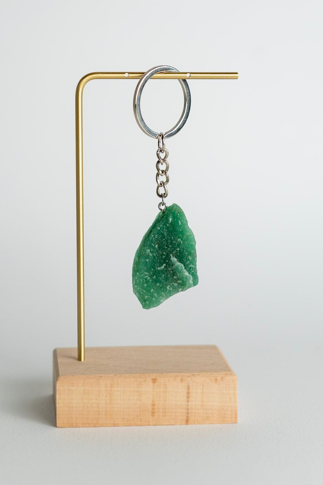 Green stone pendant on a keychain attached to a brass stand with a wooden base on a light gray background