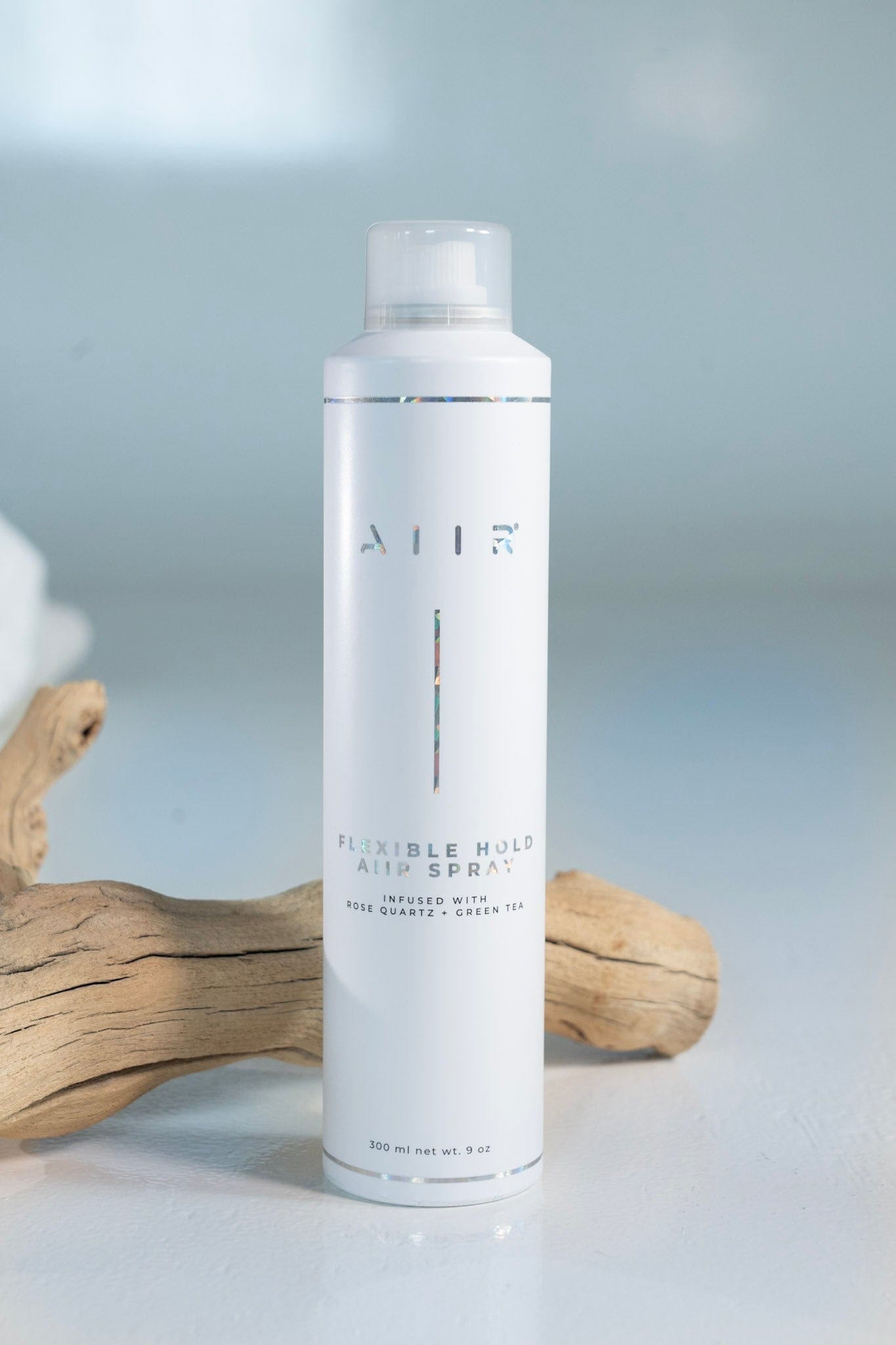 White hair spray bottle labeled 'AIR' on a light gray background with wooden driftwood.