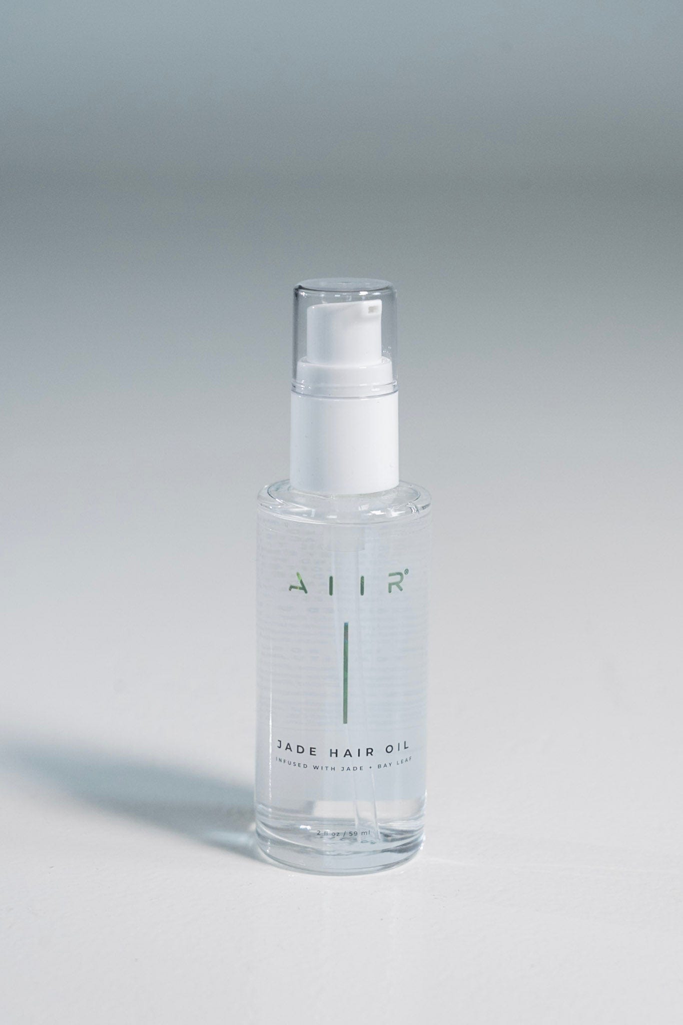 Clear bottle of hair oil with a white cap on a gray background