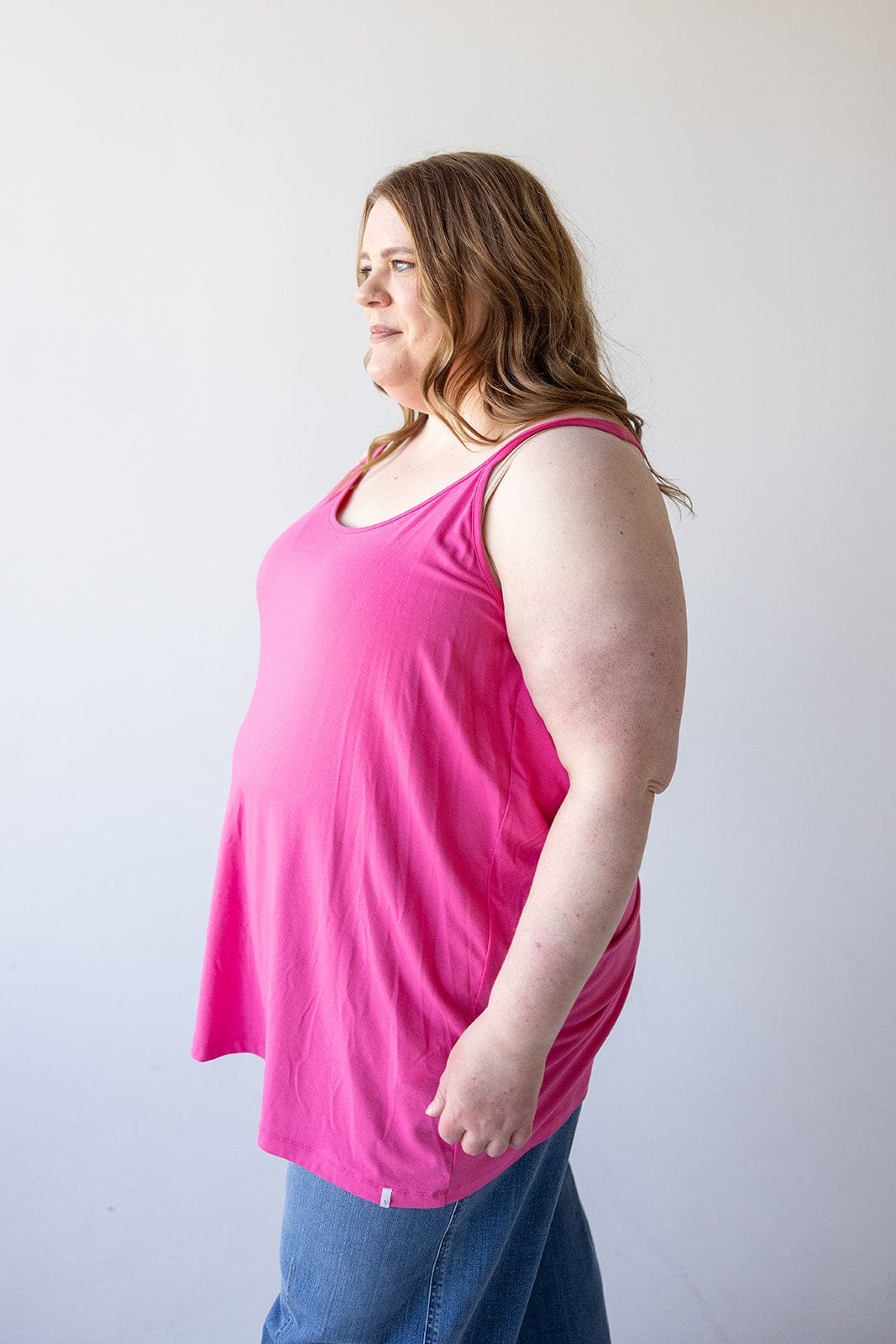 A woman wearing a Love Marlow BASIC RACERBACK CAMI IN FRESH FUCHSIA and blue jeans stands in a neutral pose against a plain background, showcasing effortless versatility.