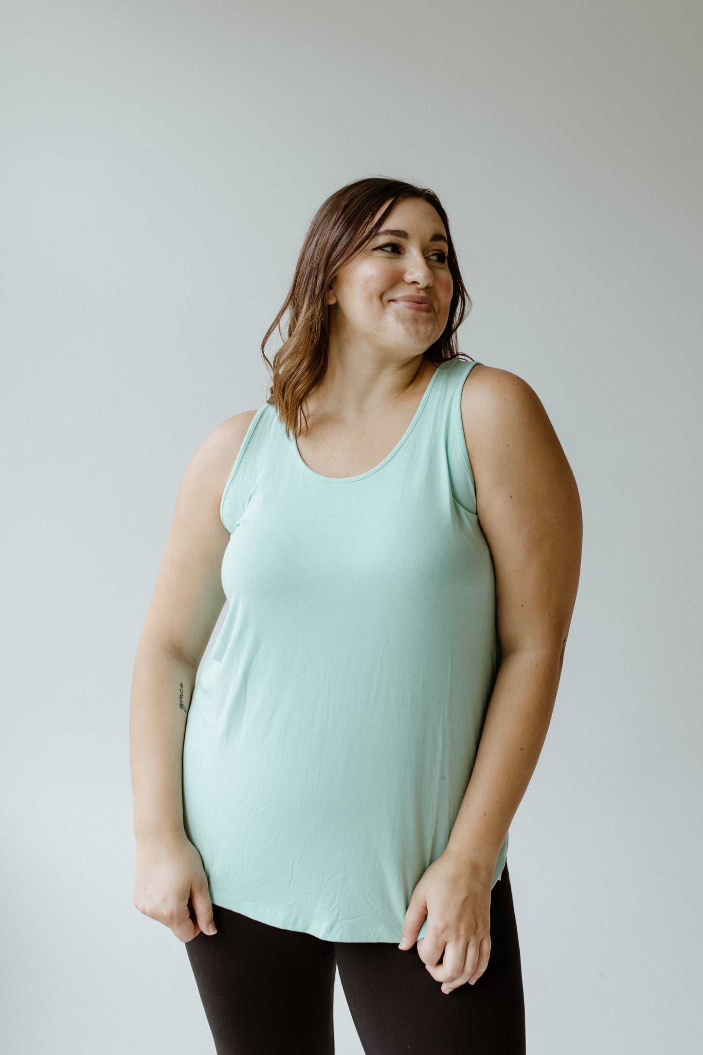 A person wearing a basic round neck tunic tank and black pants stands against a plain background. The light blue tank top, crafted from soft modal fabric, adds an effortless charm to the look.