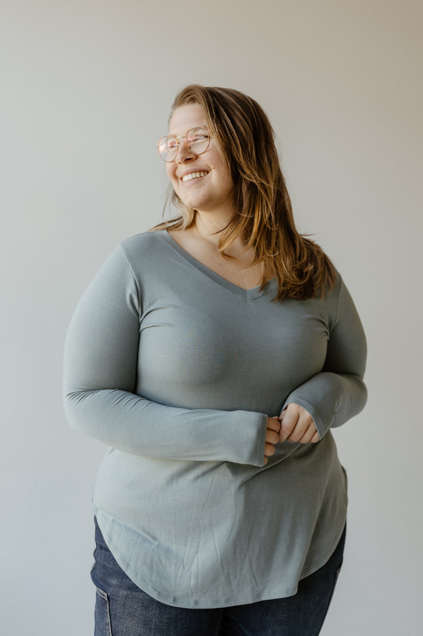 A person in glasses and a gray, super-soft fabric shirt with a subtle v-neckline smiles while looking to the side, standing against a plain background.