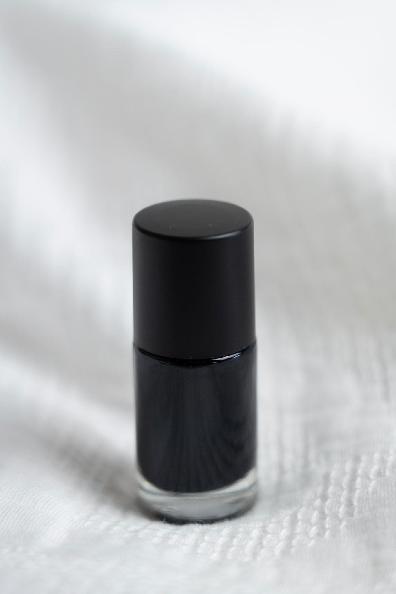 Black nail polish bottle on a white textured surface