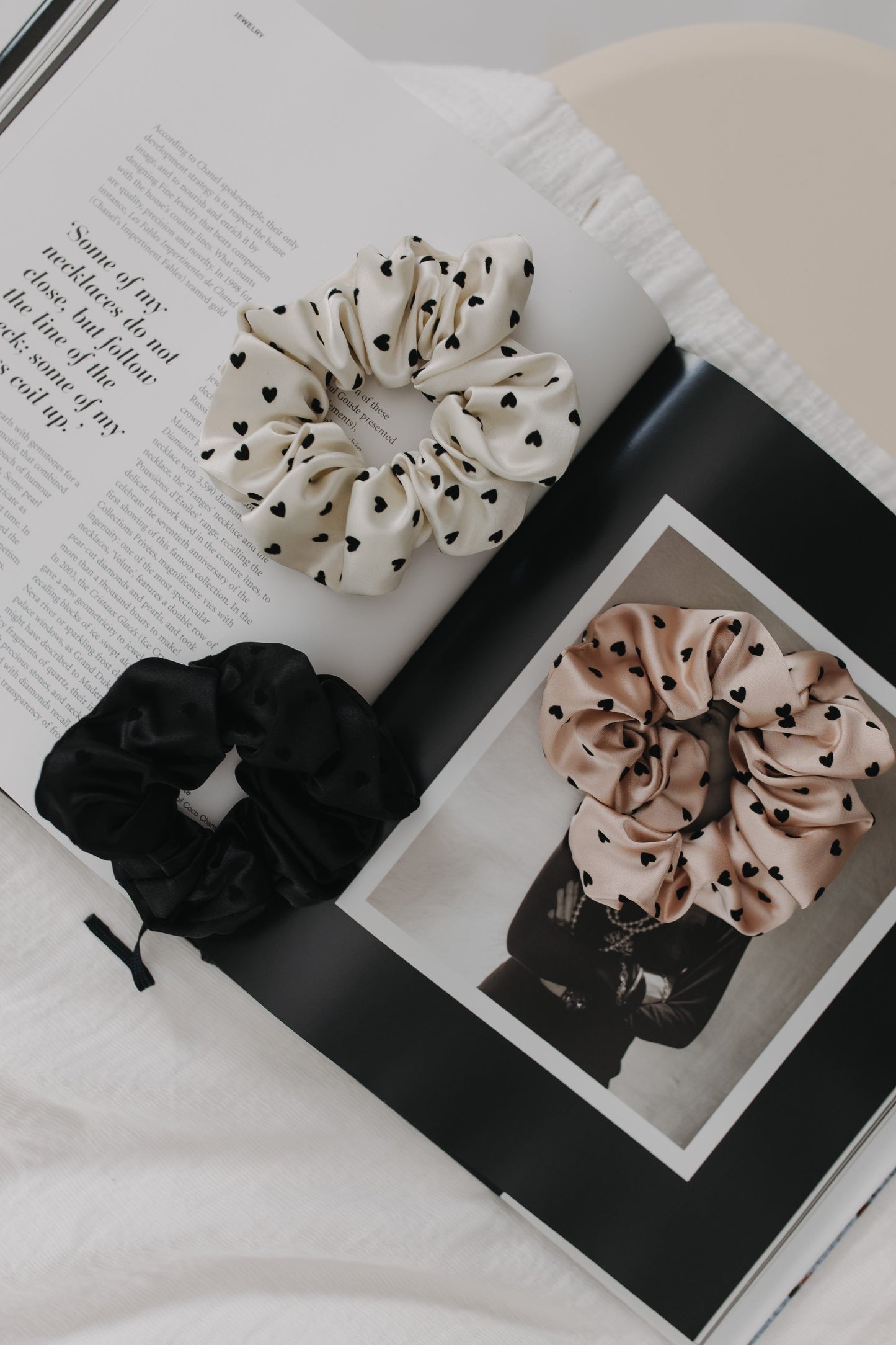 Three scrunchies (black, beige with black hearts, and white with black hearts) on an open book.