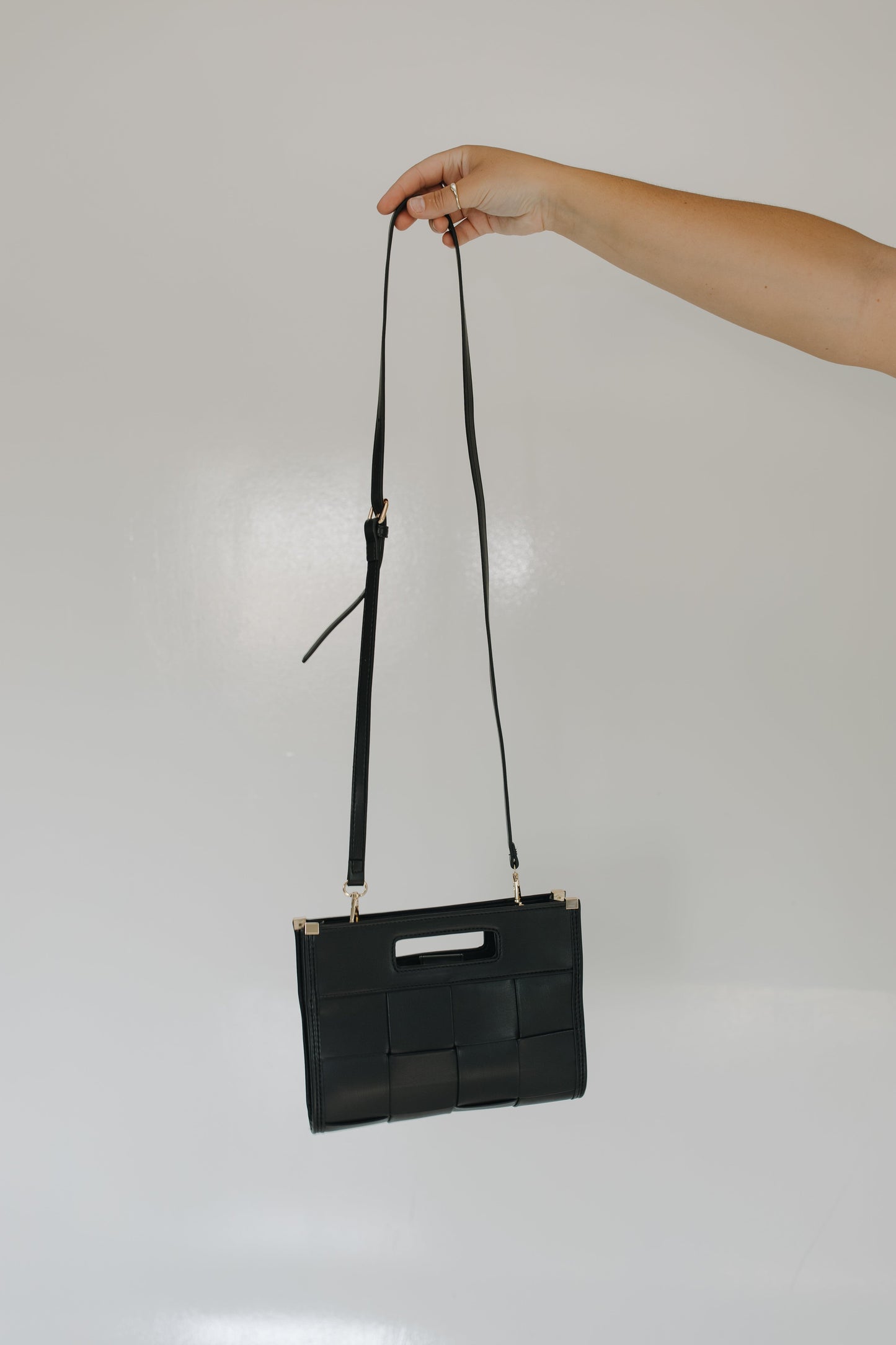 Black woven handbag with a strap held by a hand against a plain background
