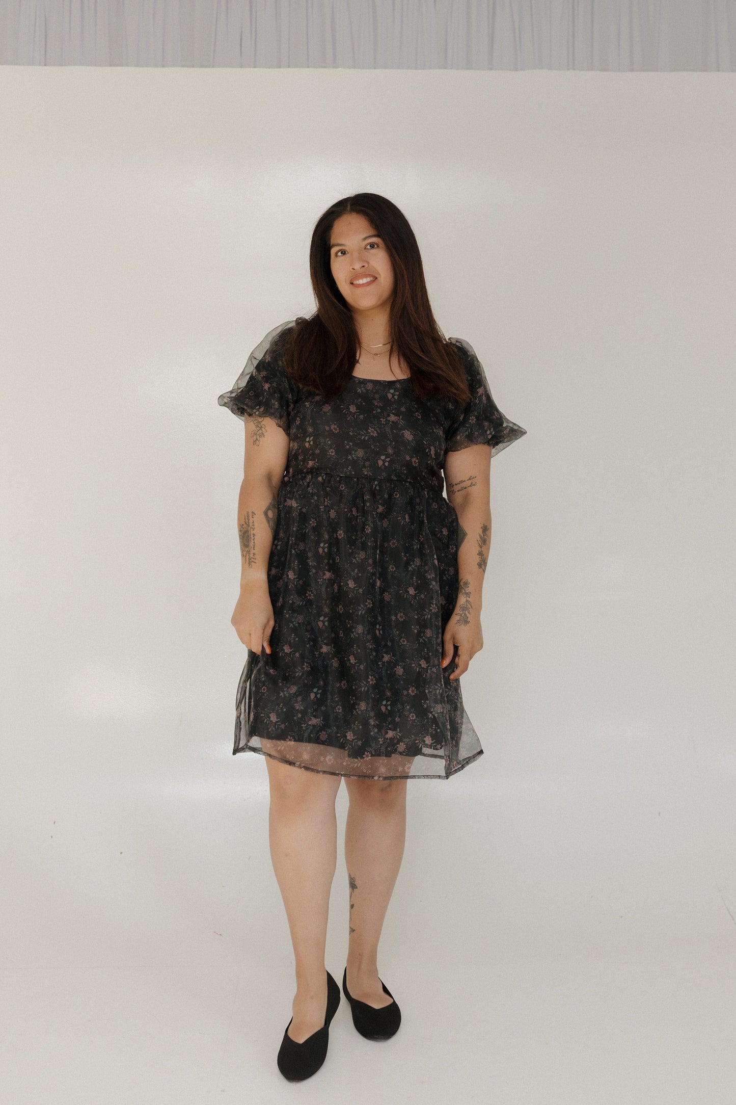 Woman wearing a black floral dress against a plain background