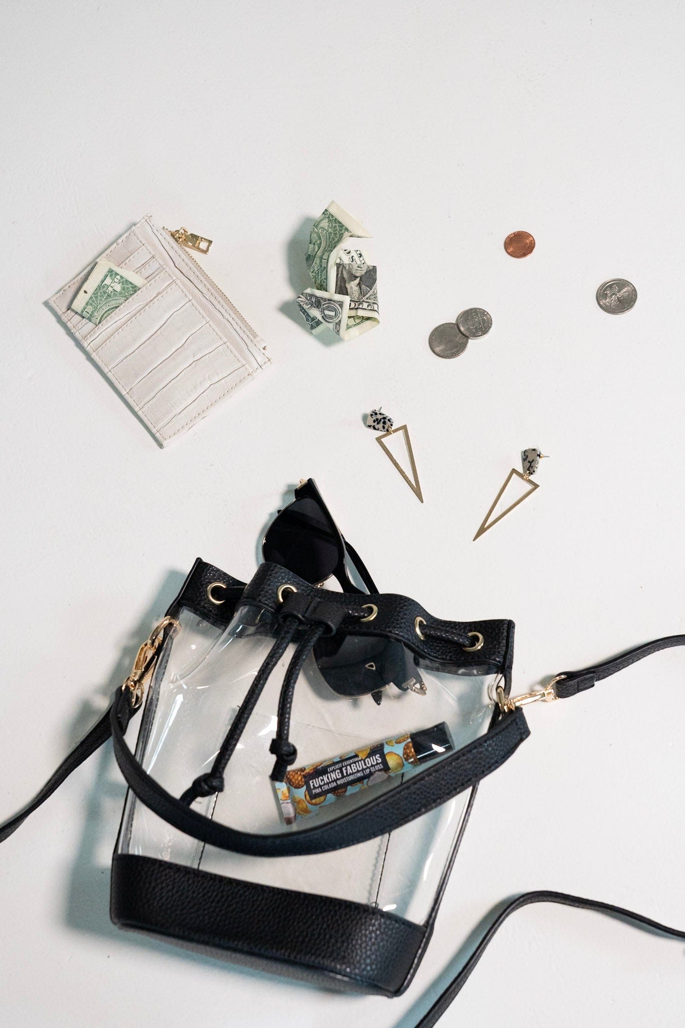 Clear handbag with black accents containing small items on a light gray background