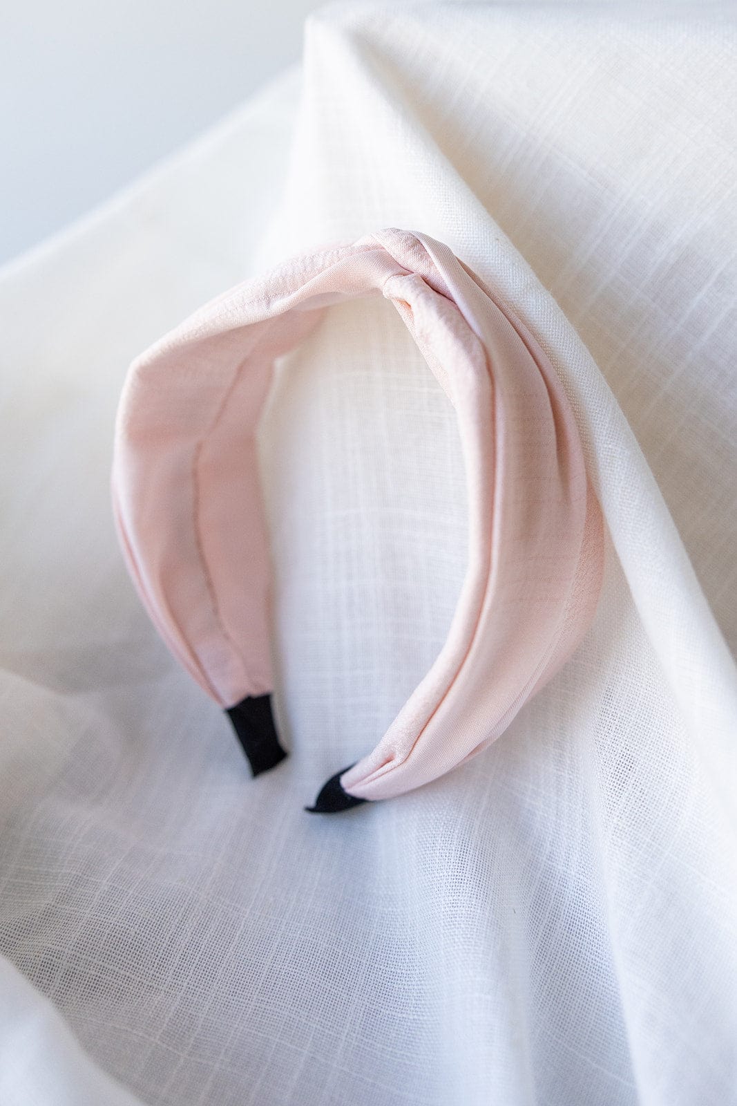 A Love Marlow CRINKLE TEXTURE HEADBAND WITH KNOT IN FRESH PINK with black ends is placed on a white, textured cloth background. Made from flexible material, this stylish accessory also comes with free standard shipping.
