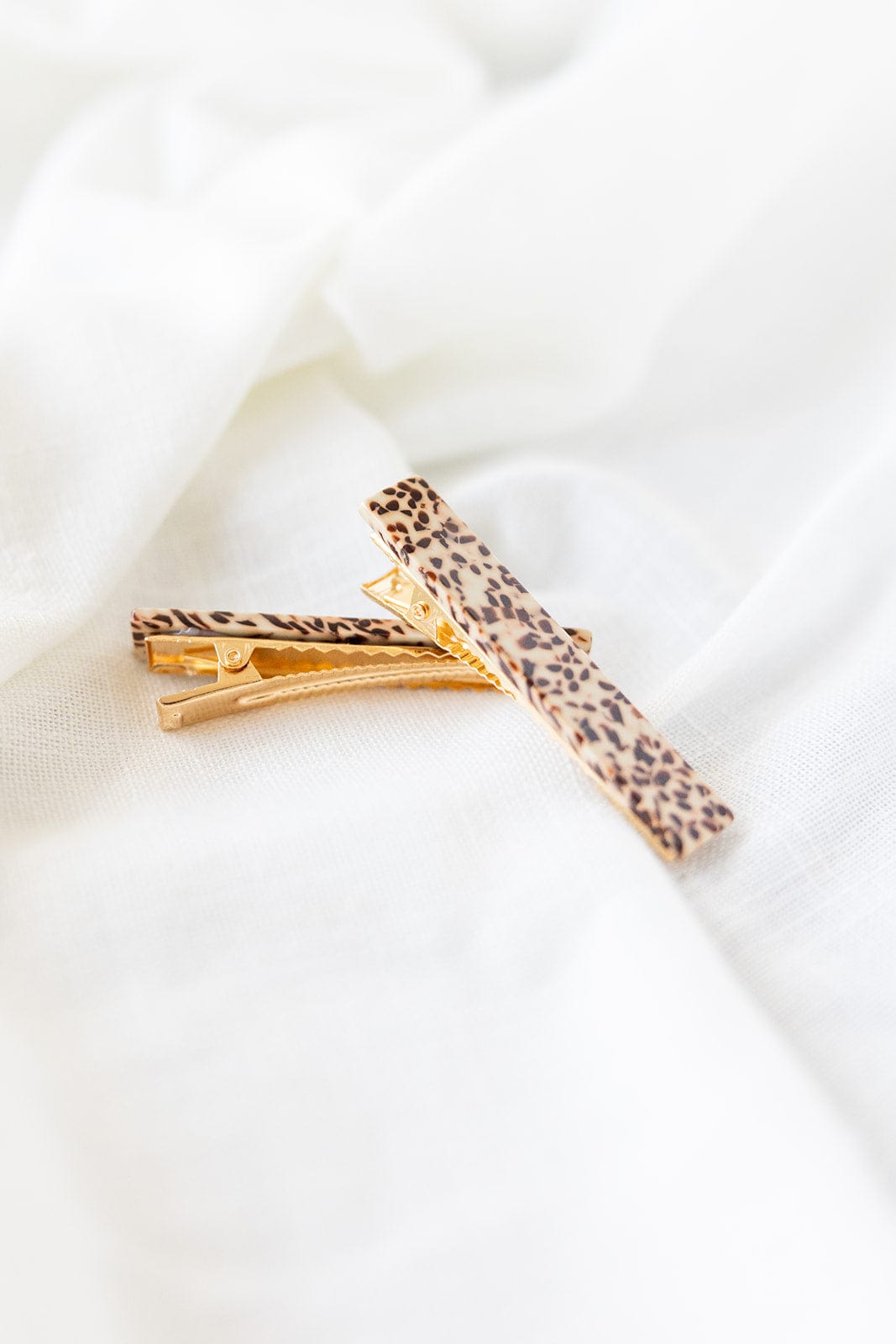 The Eleanor Hair Clips feature a striking leopard print design, crafted from plant-based acrylic, elegantly displayed on a white fabric background.
