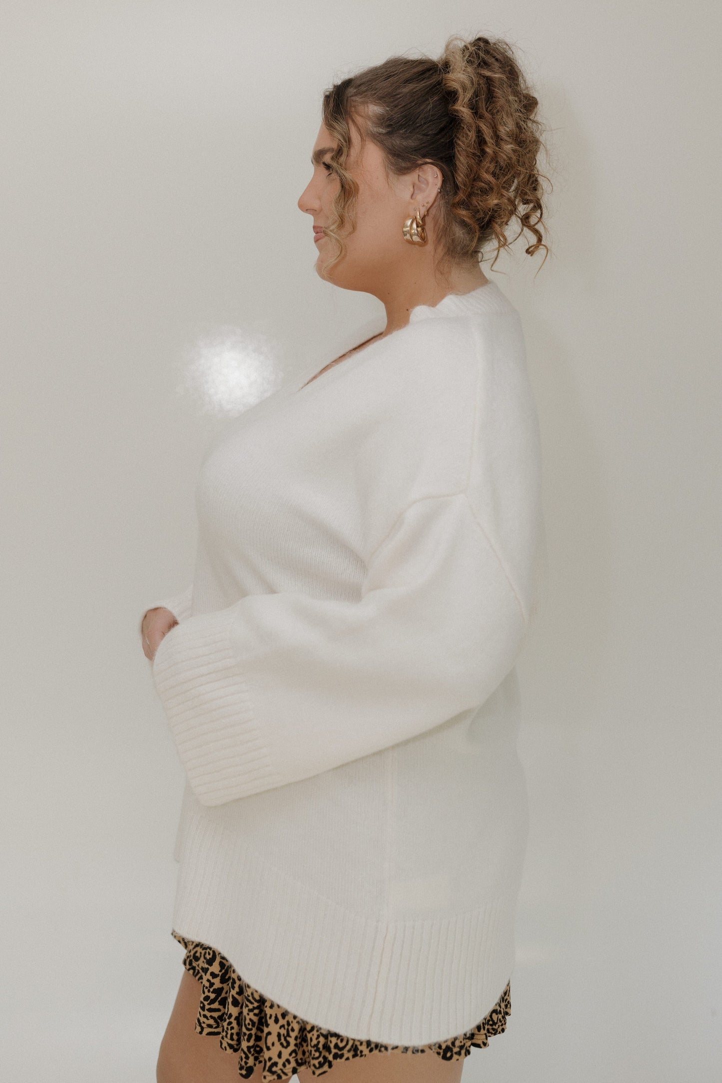 Woman wearing a white sweater and leopard print underwear against a plain background