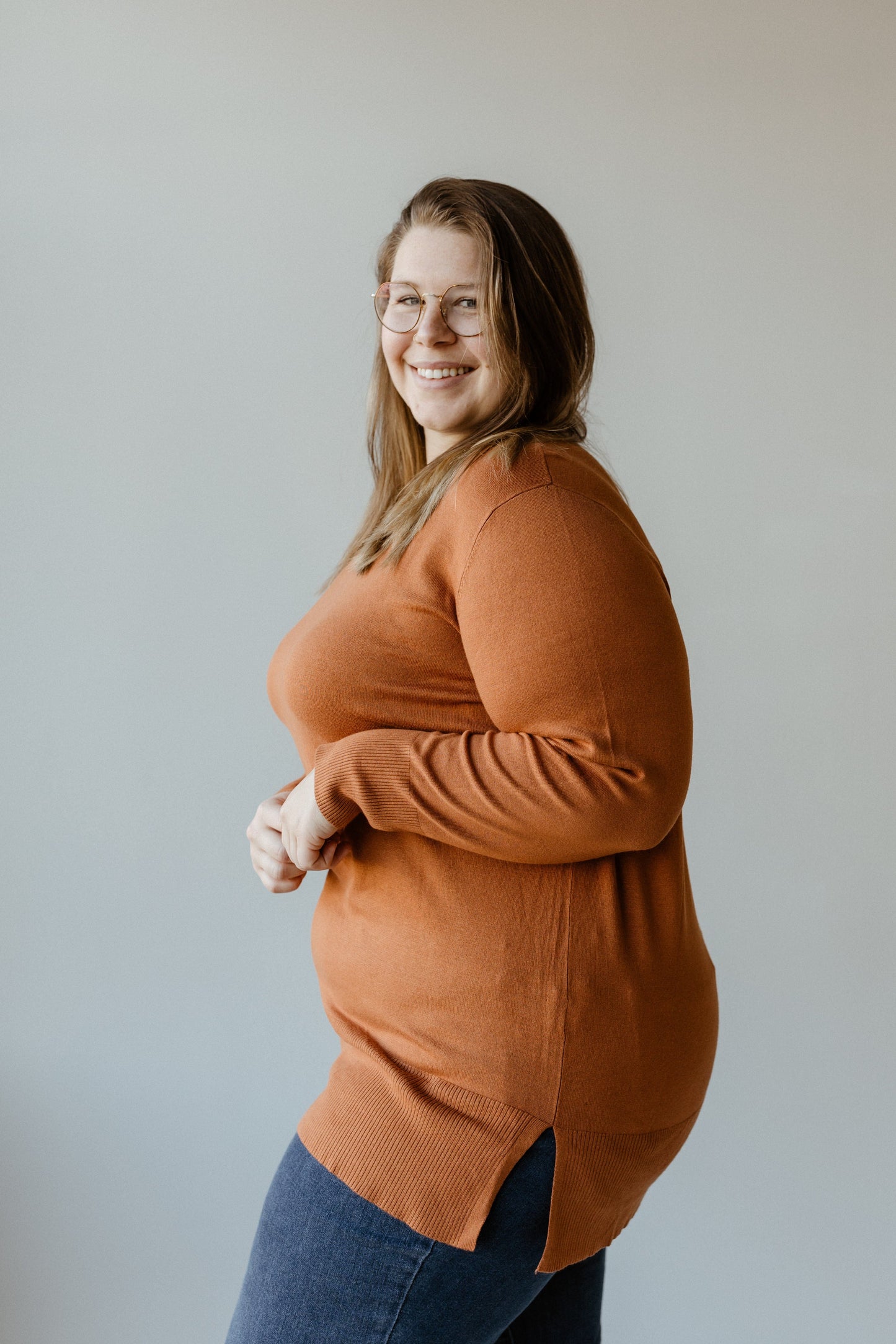 Wearing glasses and a luxury knit in Spiced Rose, the person smiles warmly while facing sideways against a neutral background.