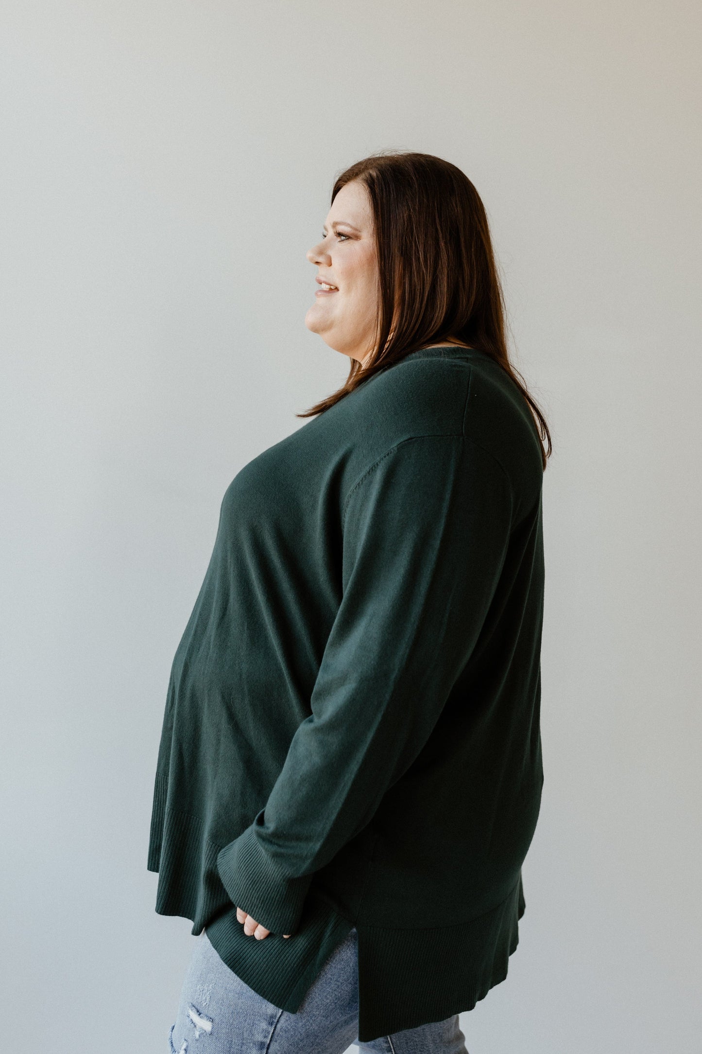 A person in an Essential Lightweight Tunic Sweater and jeans stands in profile against a plain background, exuding an air of sophistication.