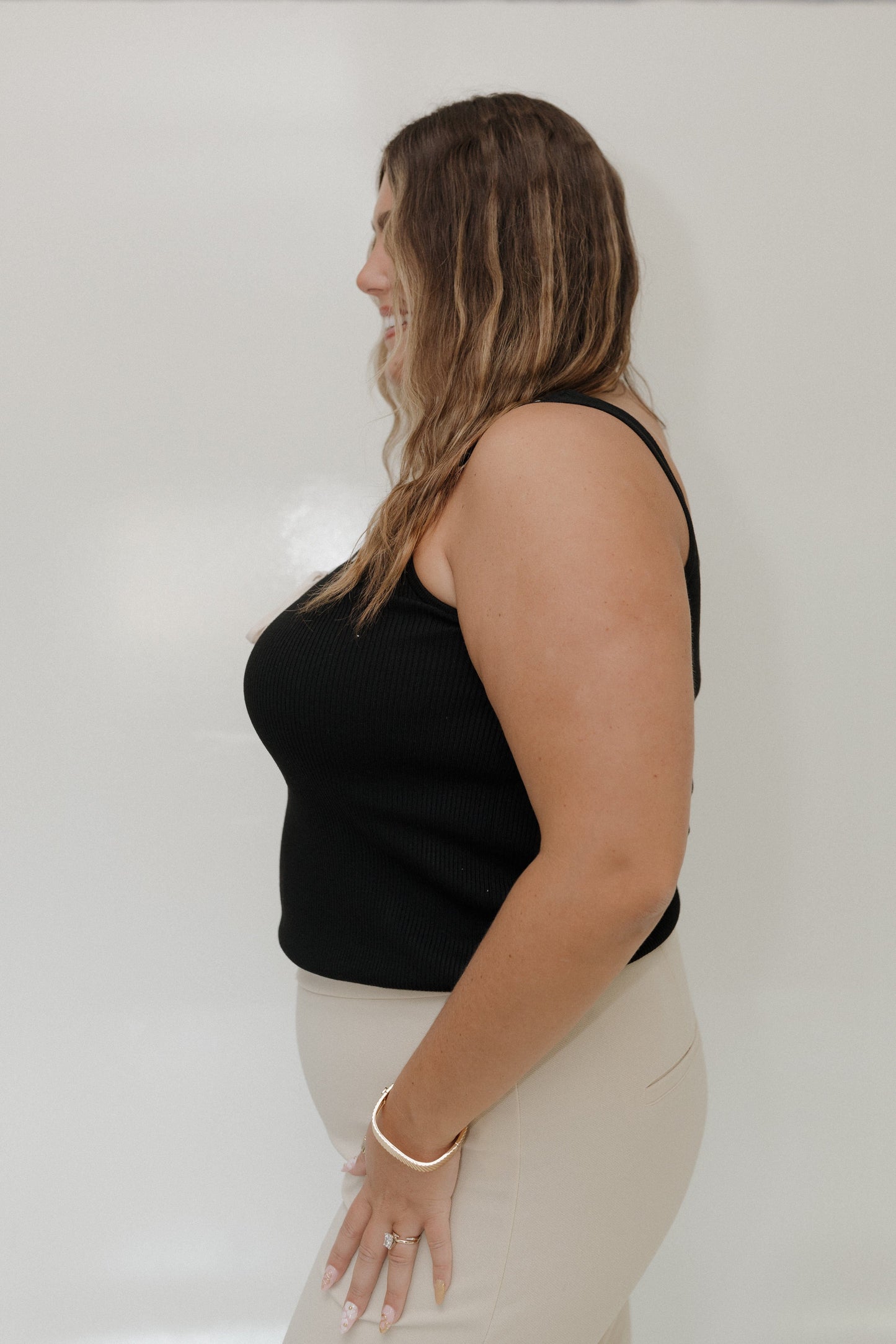 Woman wearing a black tank top and white pants against a plain background