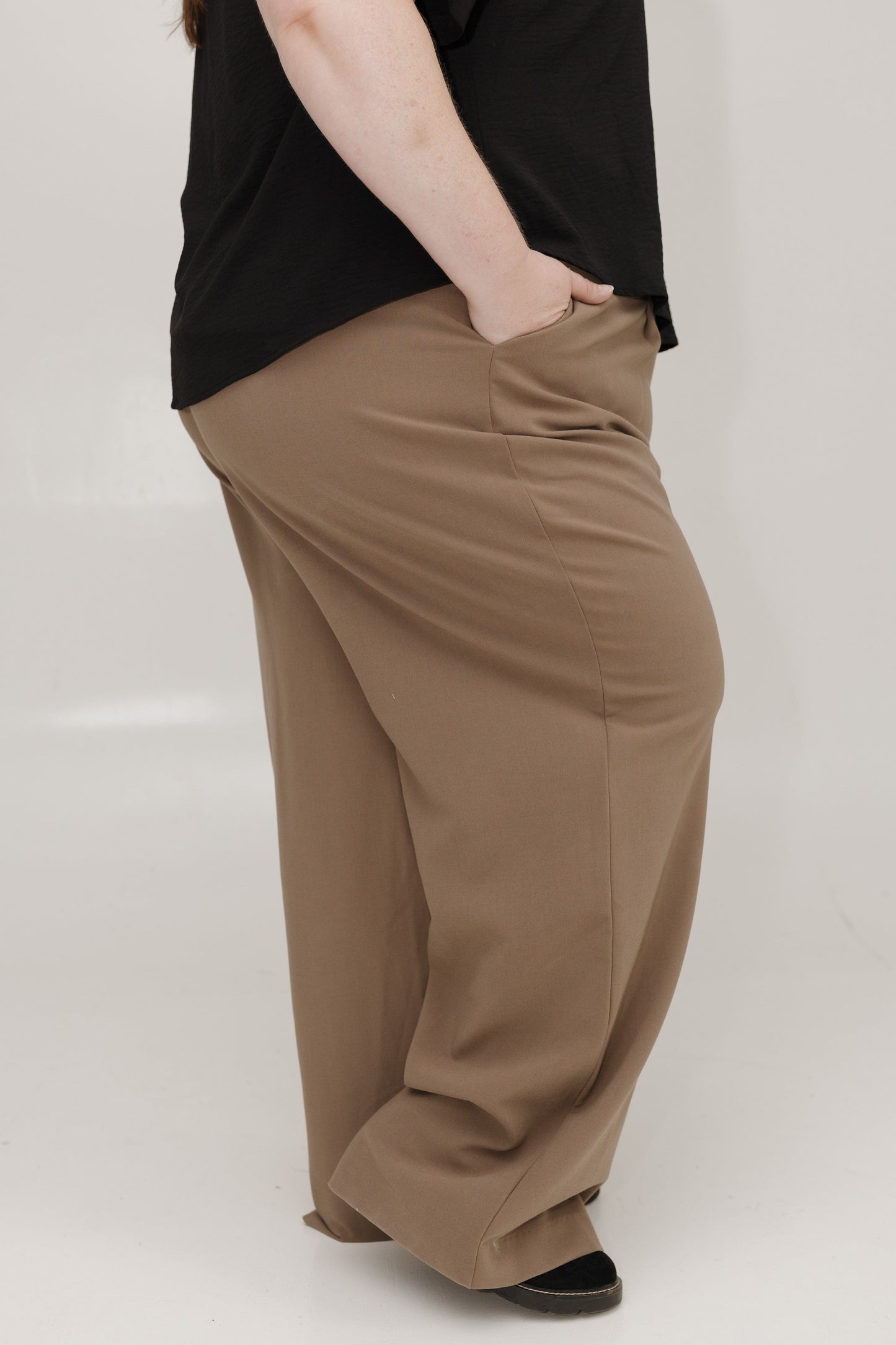 Person wearing brown wide-leg pants and a black top on a white background