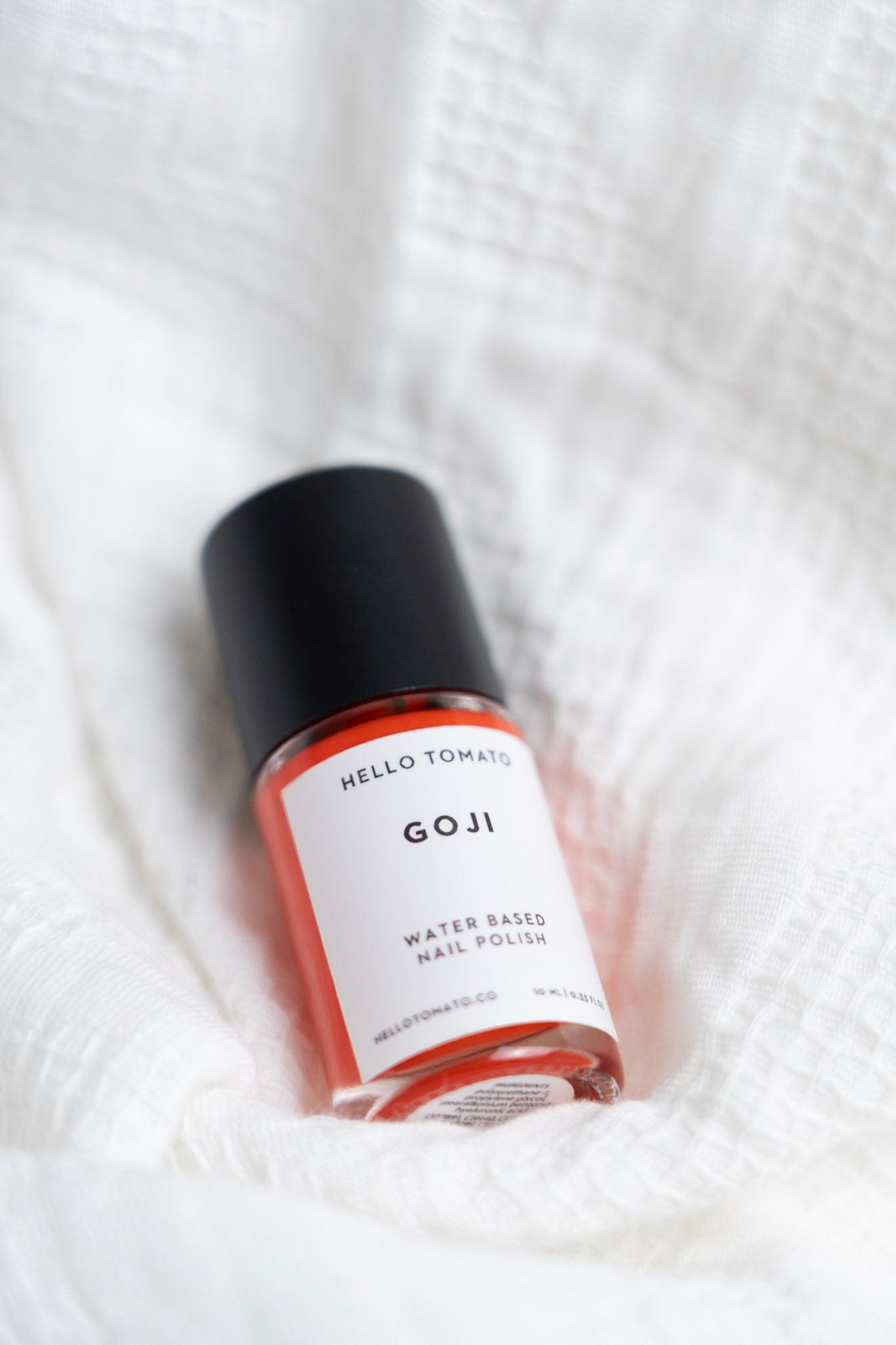 Bottle of GOJI water-based nail polish on a white textured background
