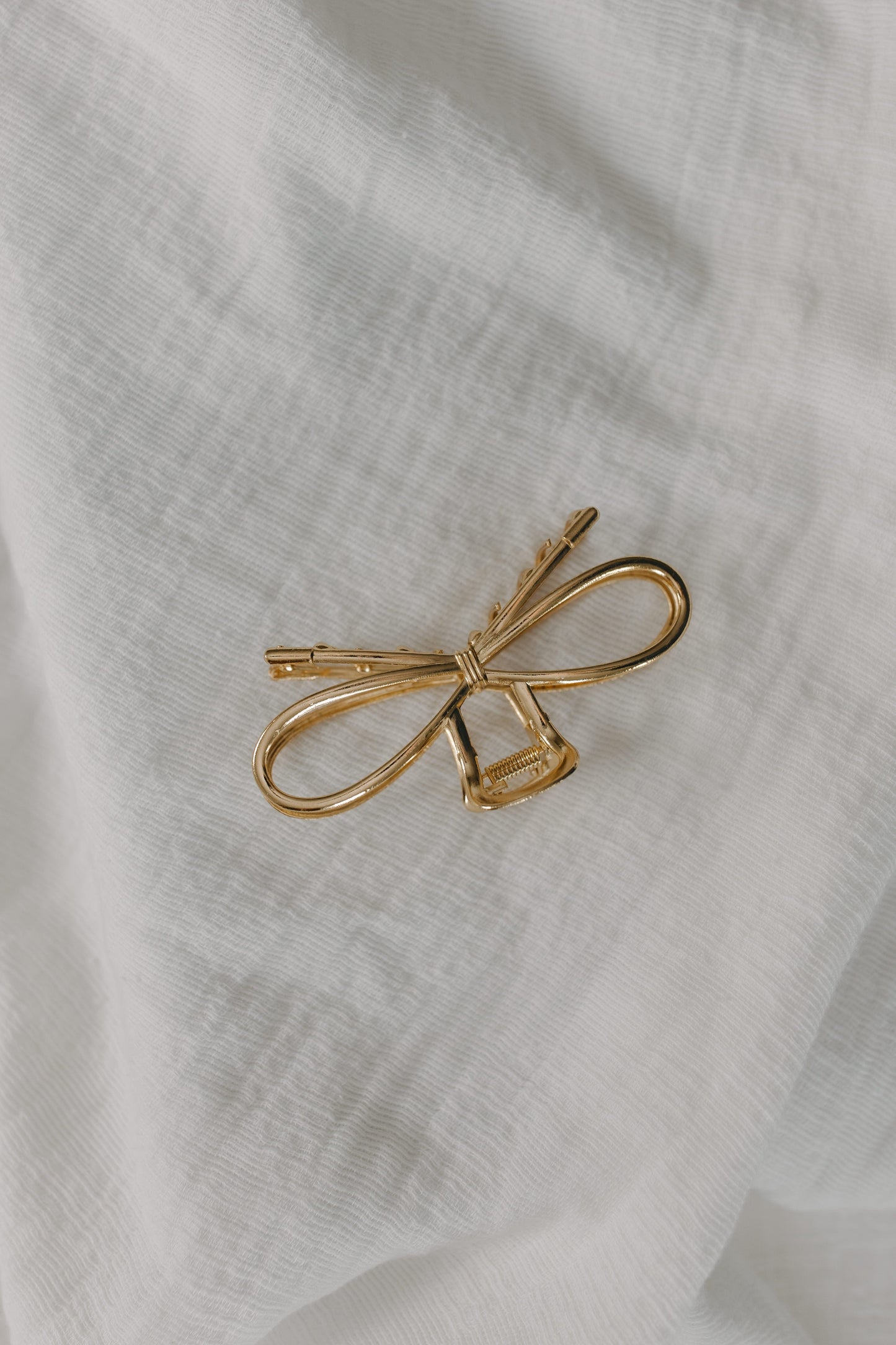 Gold bow-shaped hair clip on a white fabric background