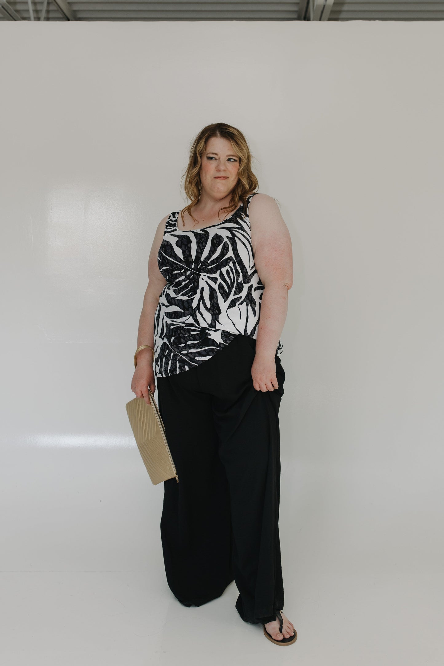 Woman wearing a black and white patterned top and black pants against a plain background