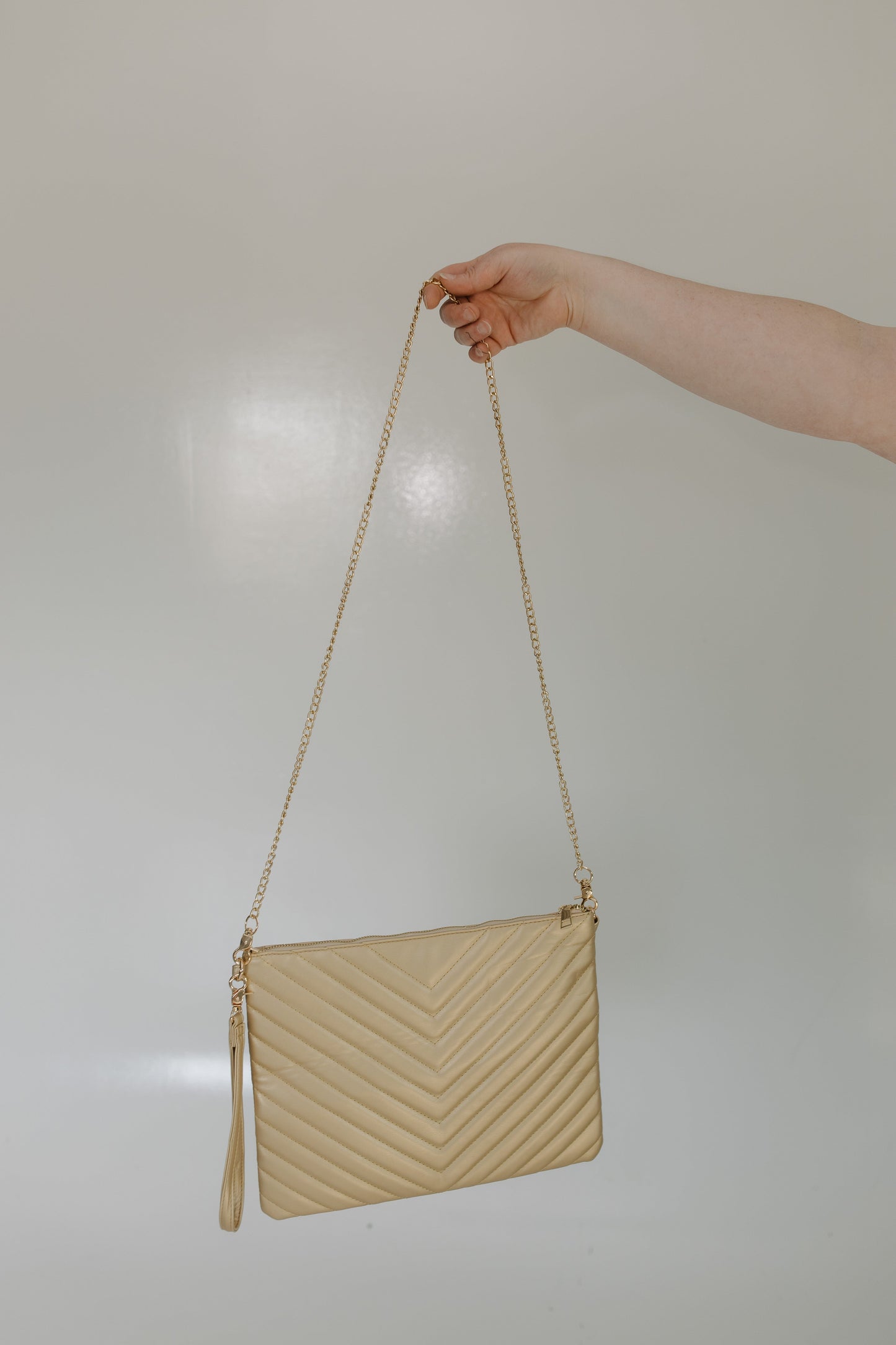 Beige handbag with a chain strap held by a hand against a neutral background