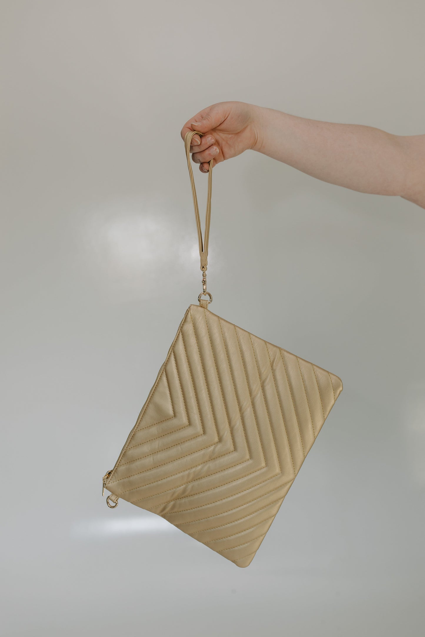 Beige handbag with a textured pattern held by a hand against a neutral background