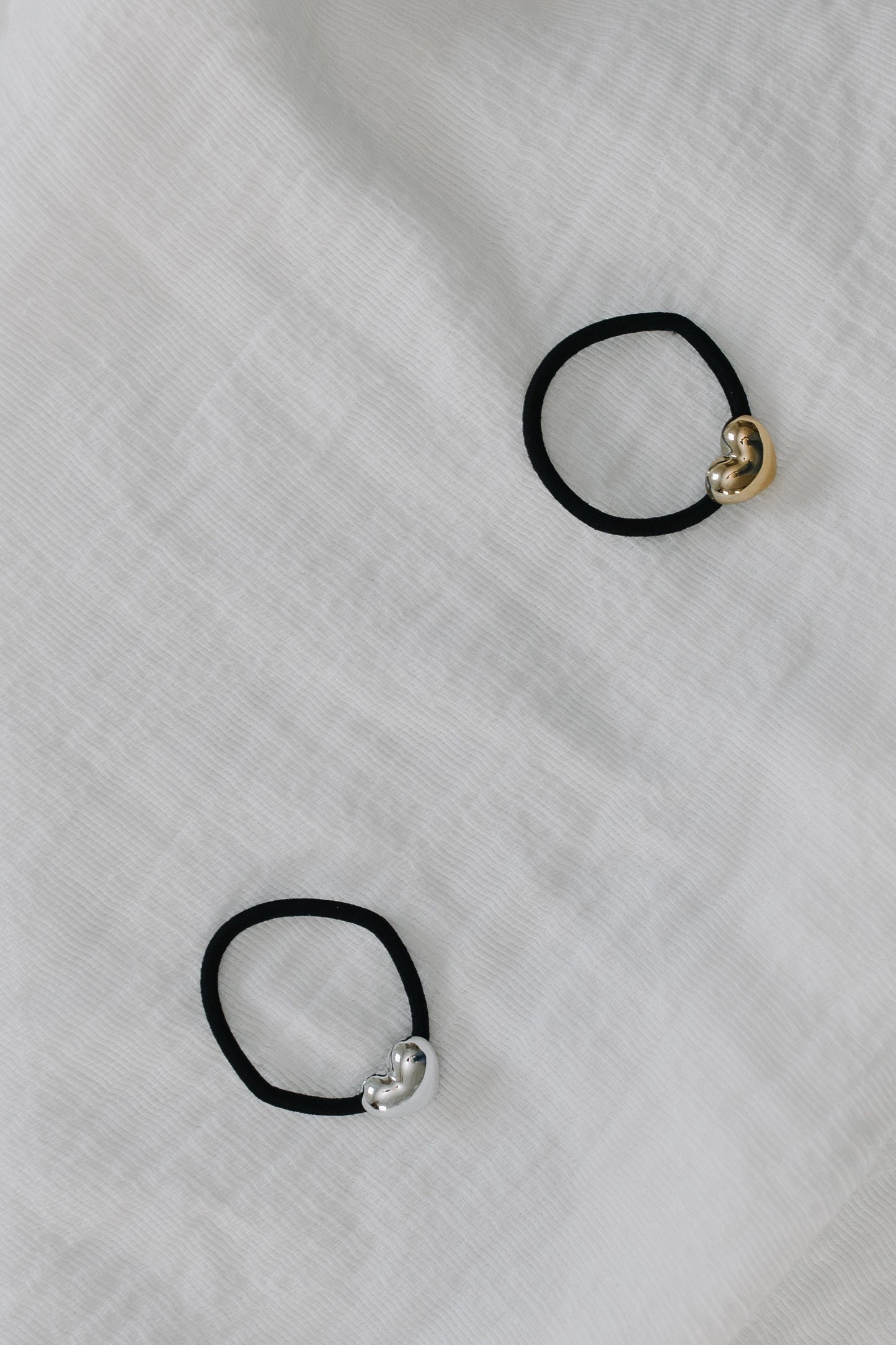 Two black hair ties with gold and silver clasp on a textured white background