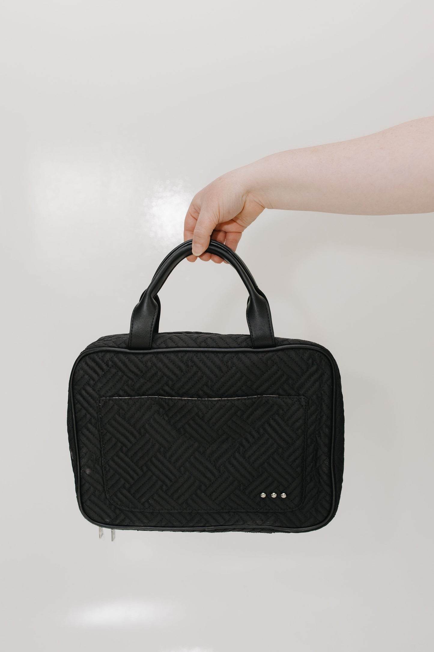 Black quilted handbag held by a hand against a light background