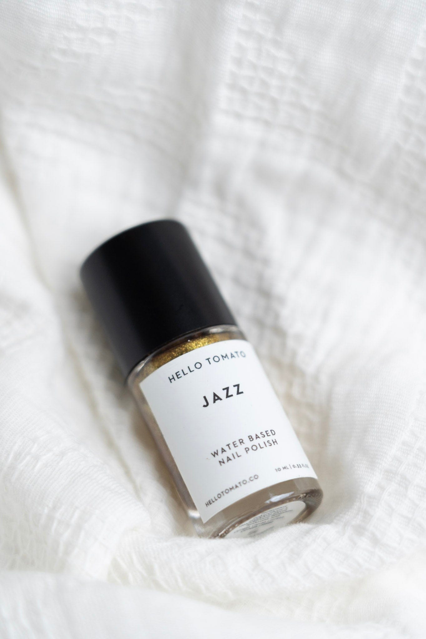Bottle of 'Jazz' water-based nail polish by Hello Tomato on a white textured background