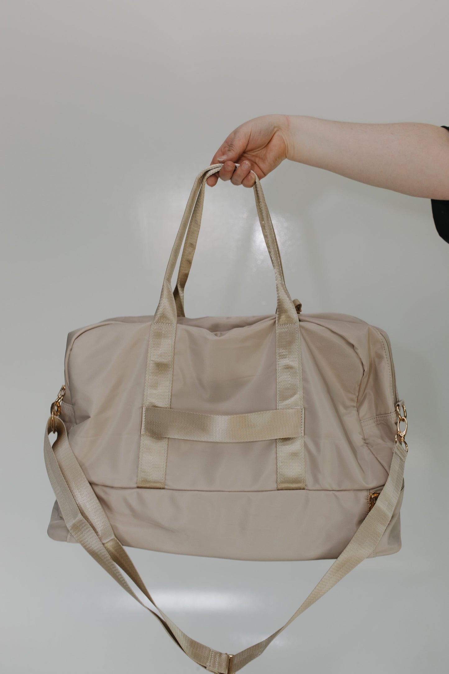 Beige duffel bag held by a hand against a plain background
