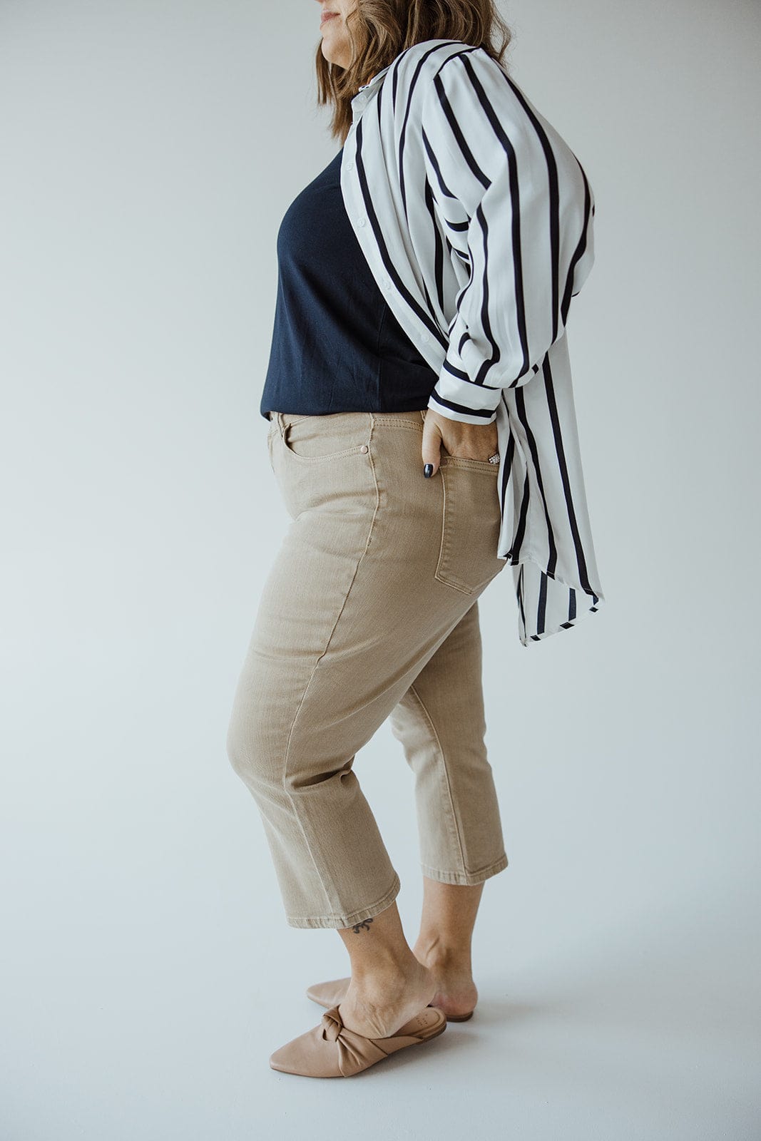 Person standing sideways wearing a blue Judy Blue top, striped overcoat, JUDY BLUE NON-DISTRESSED CAPRI IN WASHED KHAKI by Judy Blue, and beige flats against a plain backgroundāa perfect summer style ensemble.