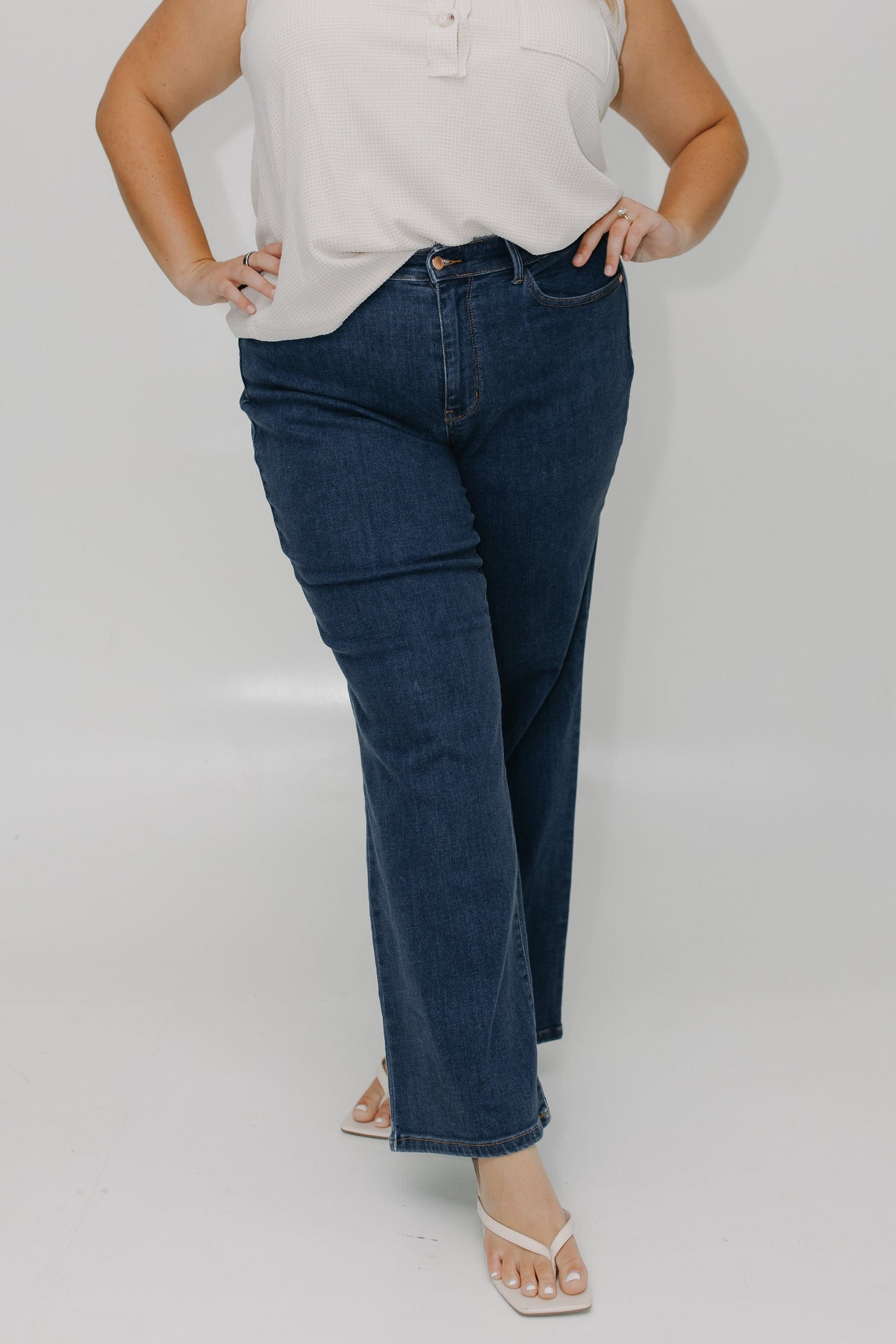 Woman wearing a white sleeveless top and blue jeans against a plain background
