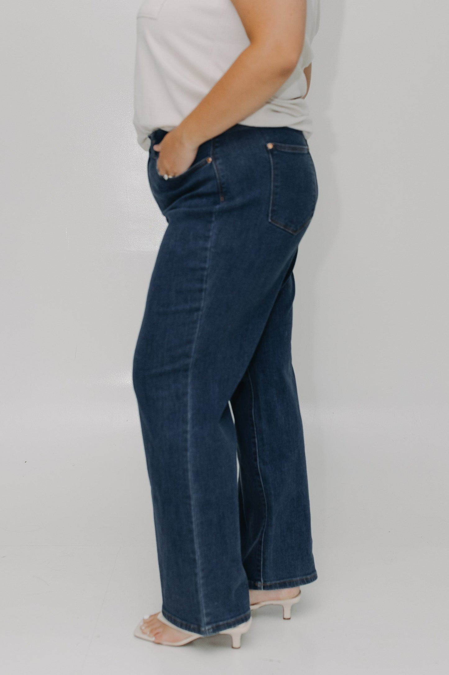 Person wearing blue jeans and a white top on a plain background