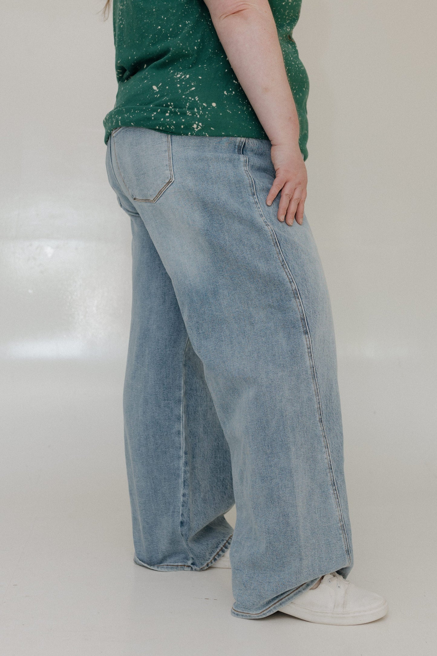 Person wearing light blue jeans and a green top on a white background