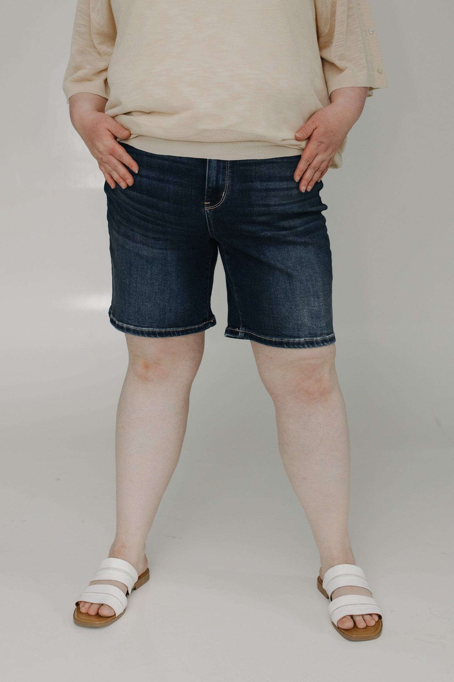 Person wearing blue denim shorts and a beige top on a plain background