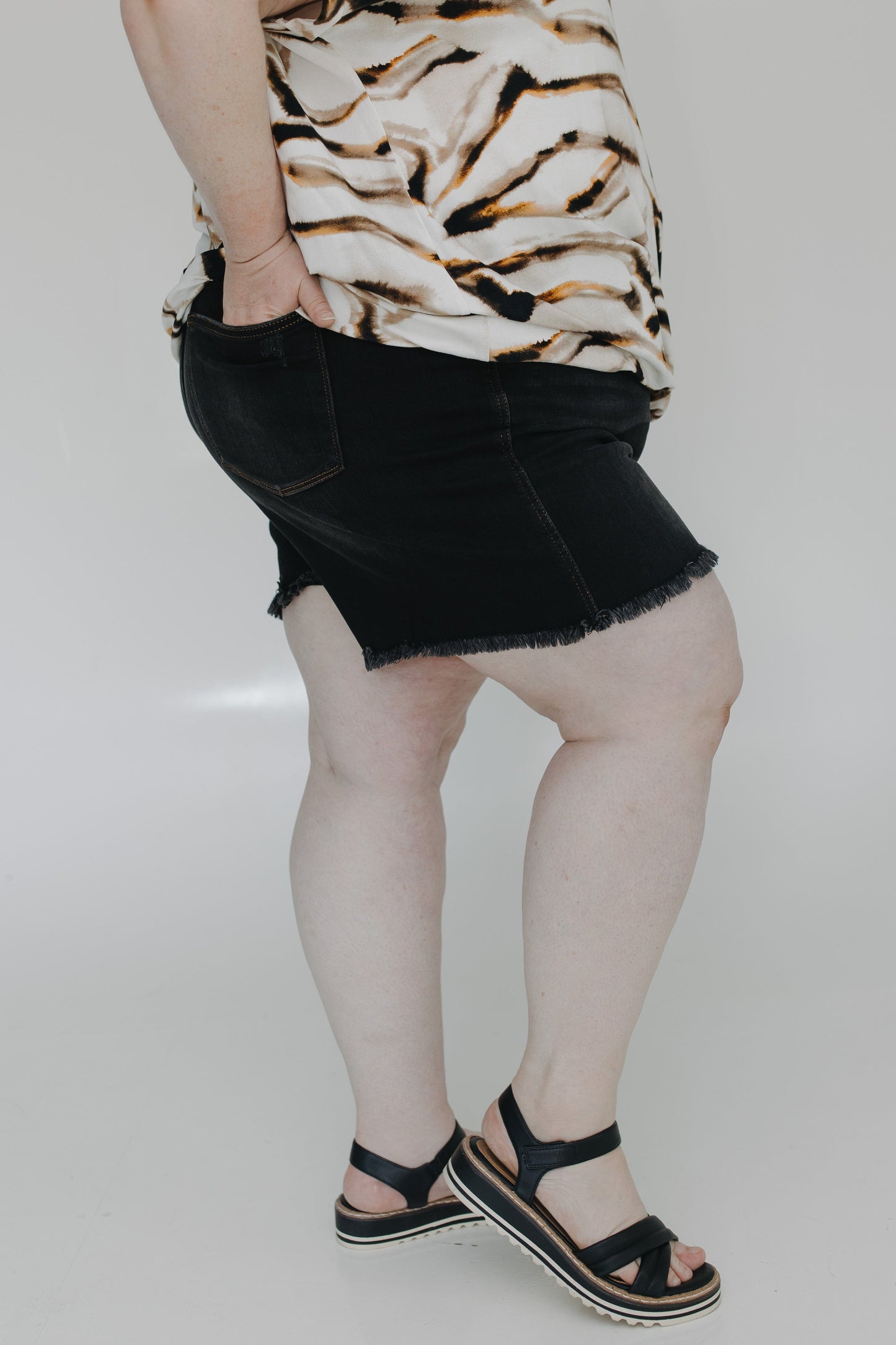 Person wearing a tiger print top and black denim skirt on a plain background