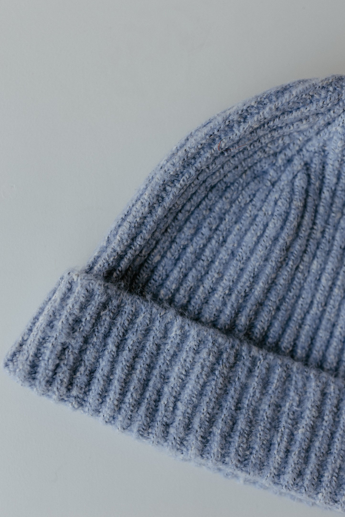 A close-up of a cozy knit stocking hat in light gray, featuring a folded brim, crafted from 100% acrylic. The beanie is elegantly displayed on a plain light background, making it the perfect autumn accessory.