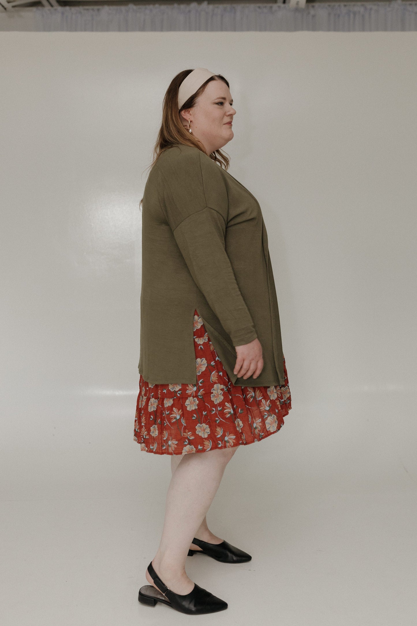 Woman wearing a green cardigan over a red floral dress on a white background