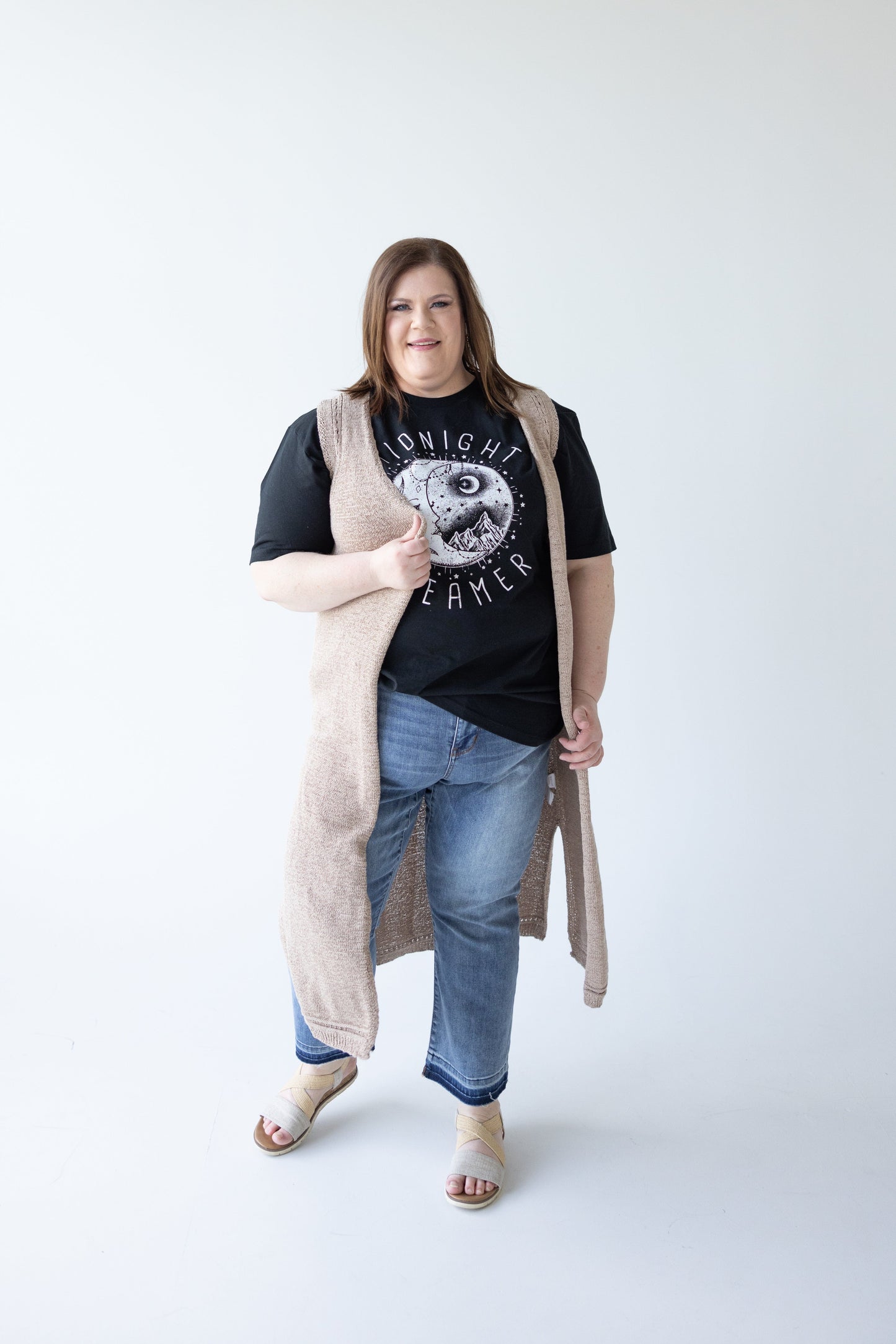 A person stands wearing a black t-shirt, jeans, the Yesta OPEN WEAVE DUSTER VEST, and sandals against a plain white background, showcasing a versatile addition to any mid to plus-size wardrobe.
