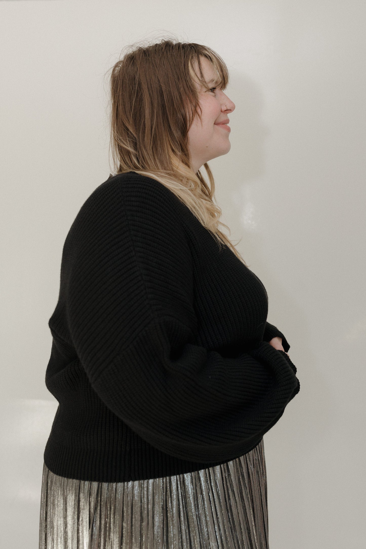 Person wearing a black sweater and pleated skirt against a plain background