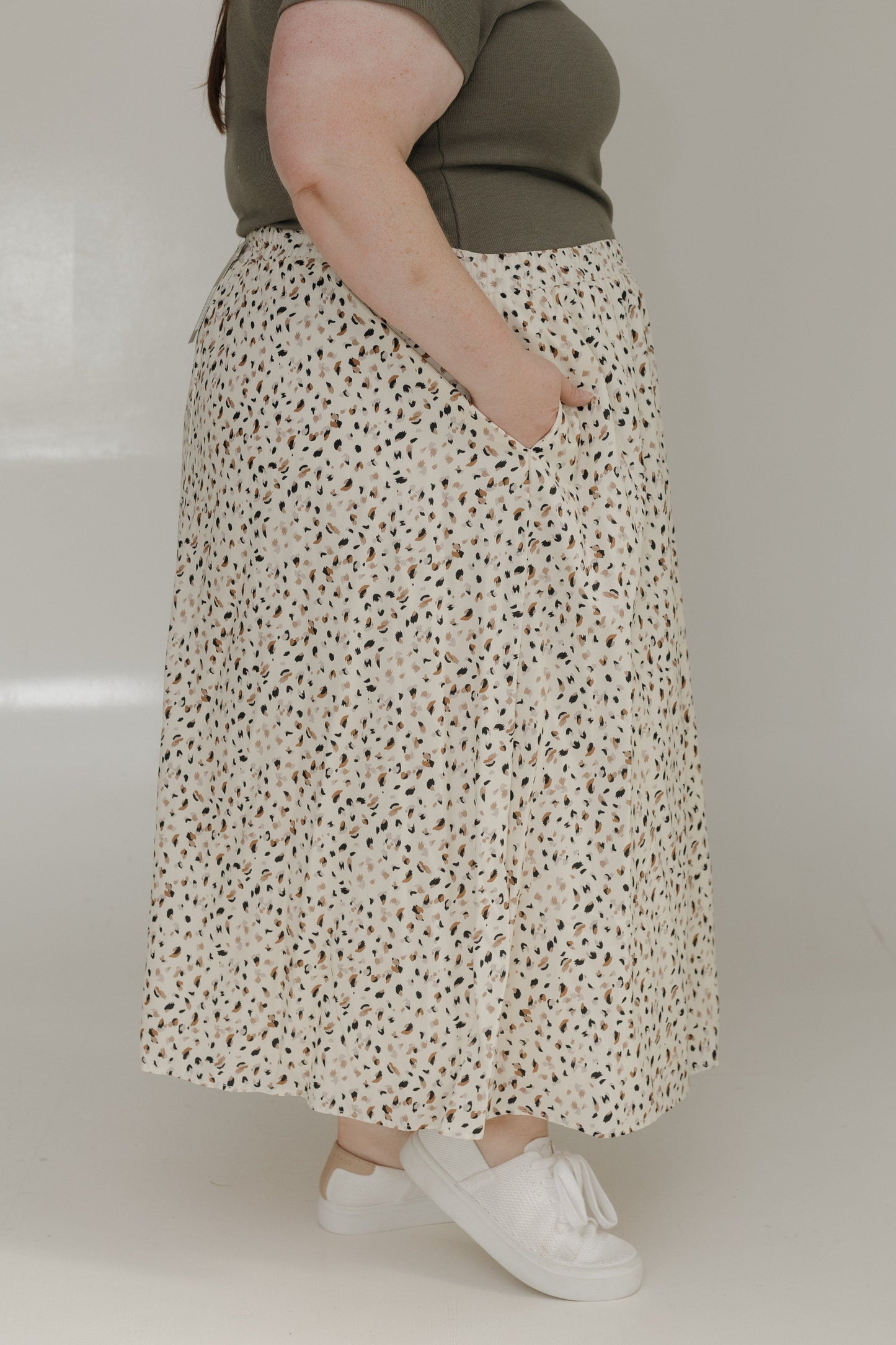 Person wearing a floral skirt and white shoes on a plain background