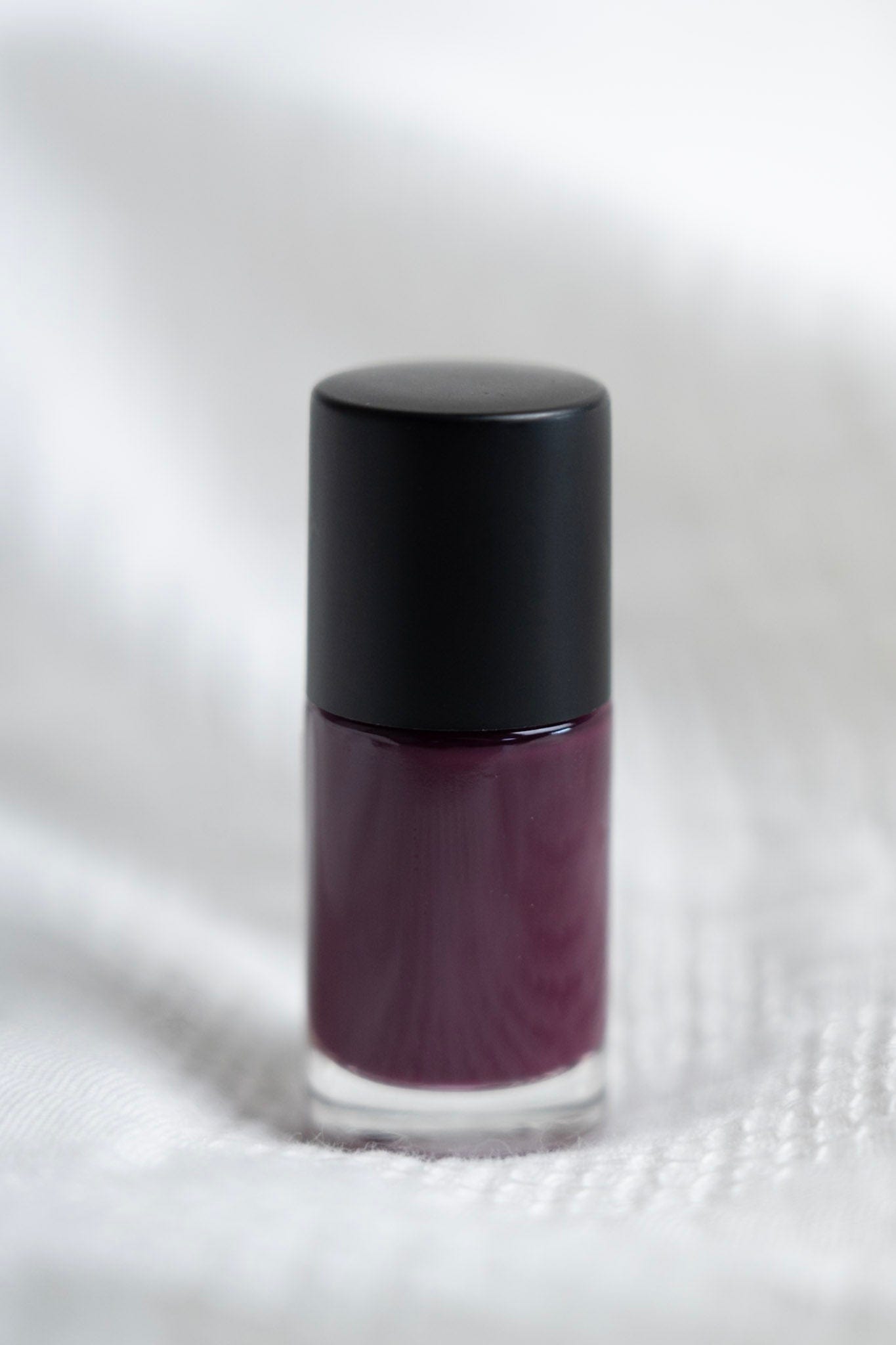 Purple nail polish bottle with black cap on a white textured background