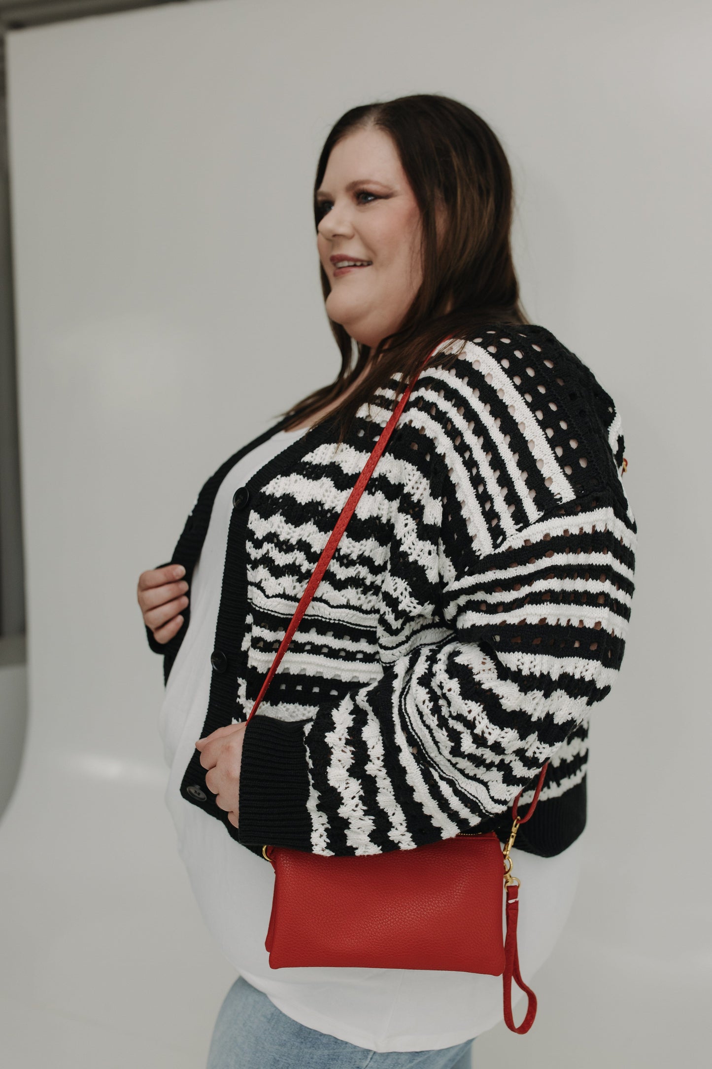 Woman wearing a black and white patterned sweater with a red handbag against a plain background