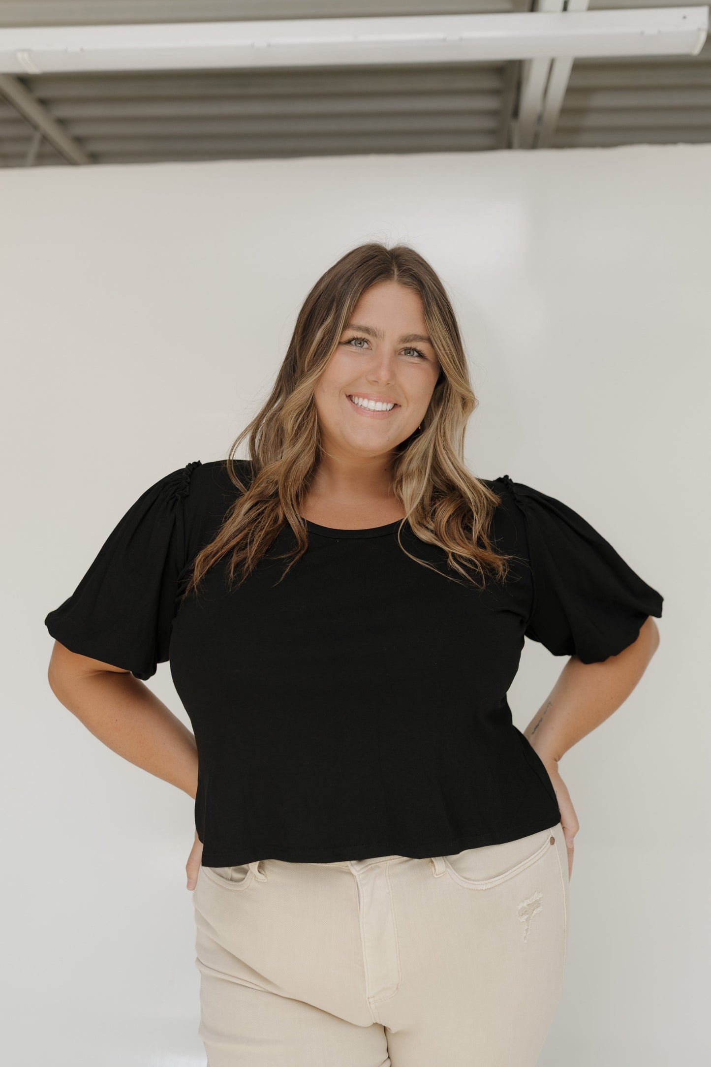 Woman wearing a black top with puffed sleeves against a white wall