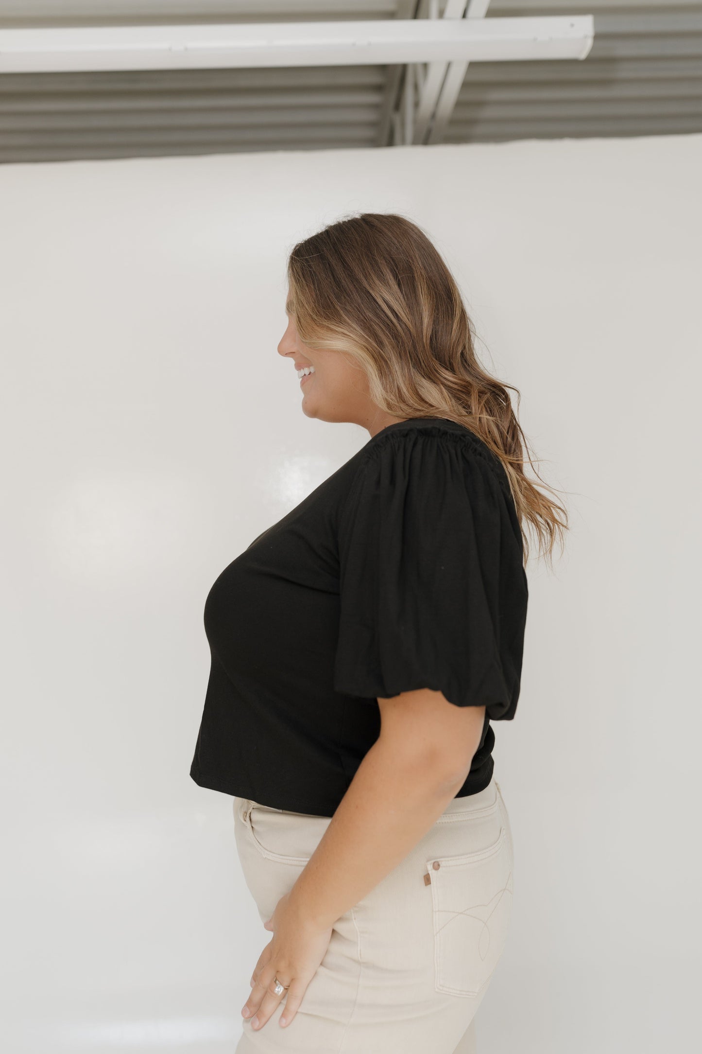 Woman wearing a black top and beige pants against a white background
