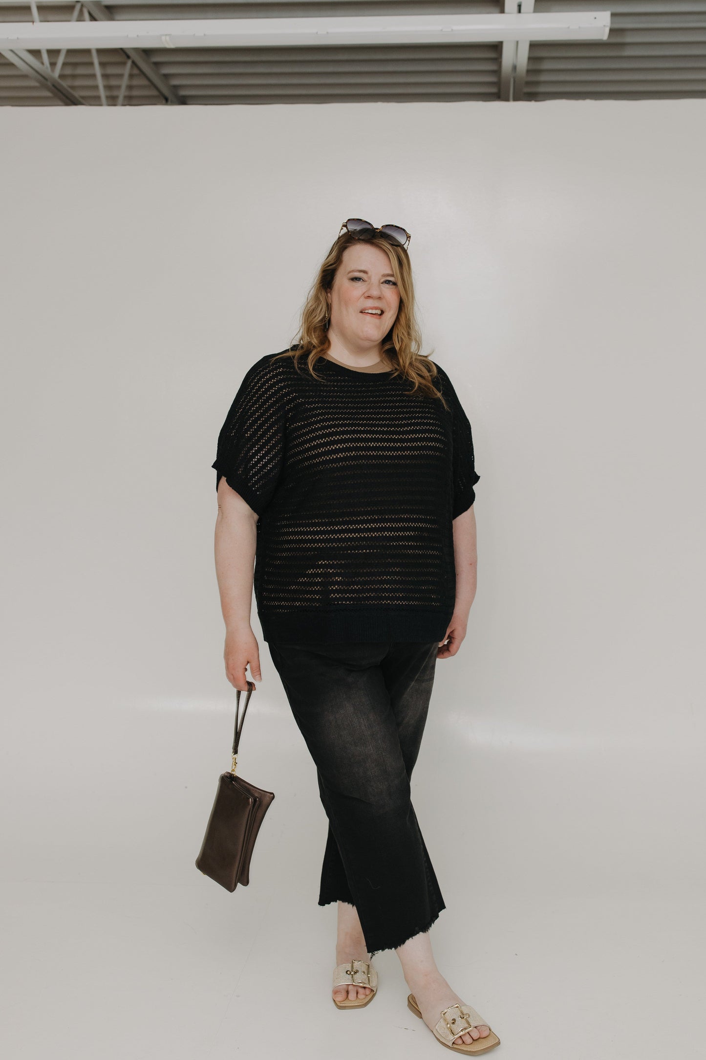 Woman wearing a black outfit holding a shimmery chocolate brown clutch with a white background