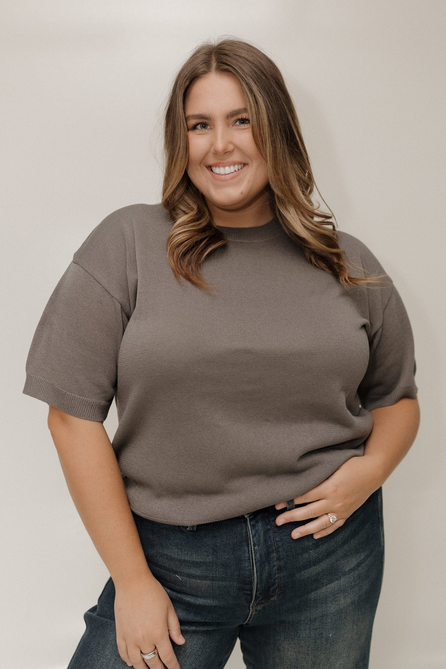 Woman wearing a brown t-shirt and jeans against a plain background