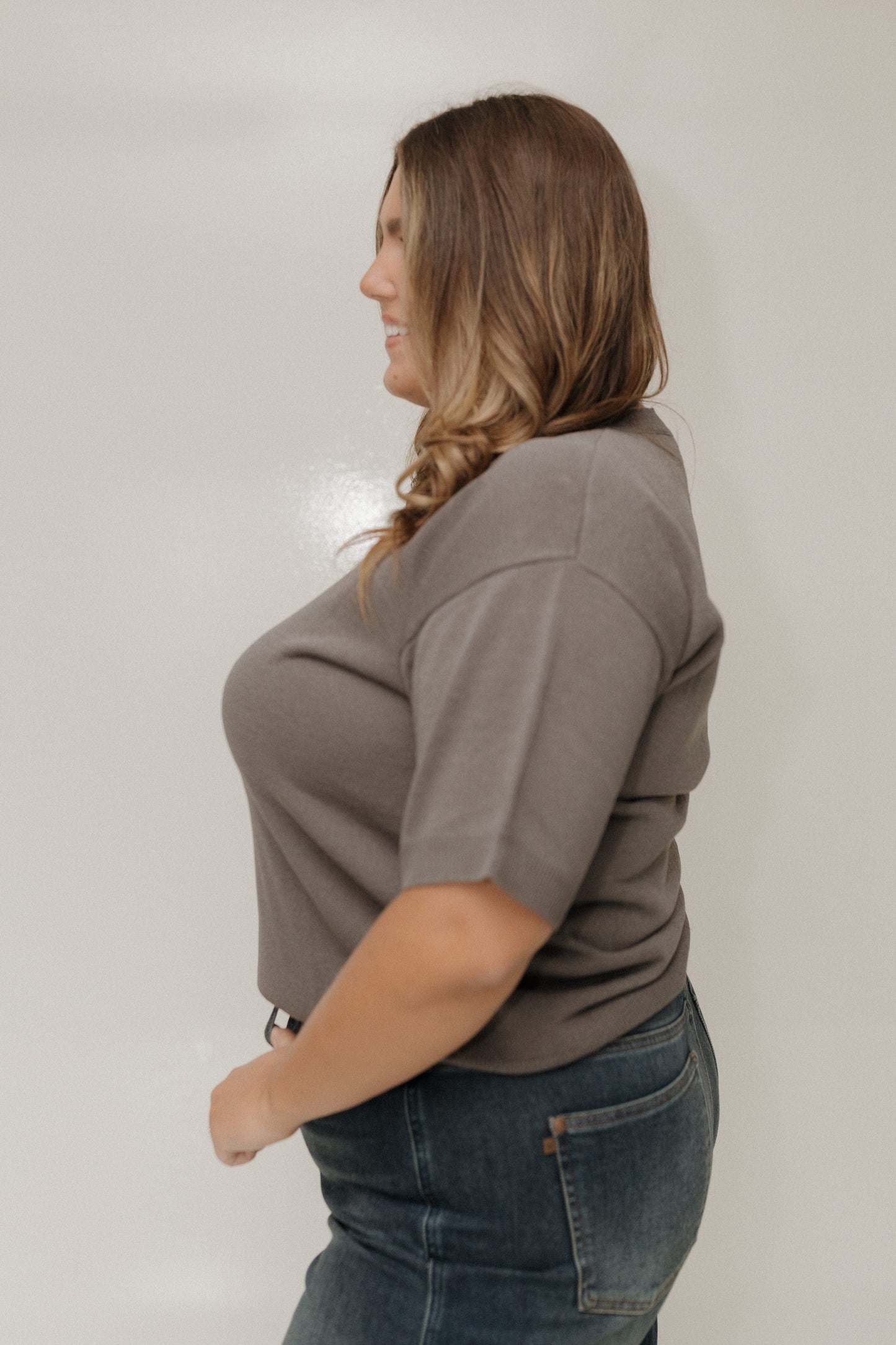 Woman wearing a brown shirt and blue jeans against a plain background