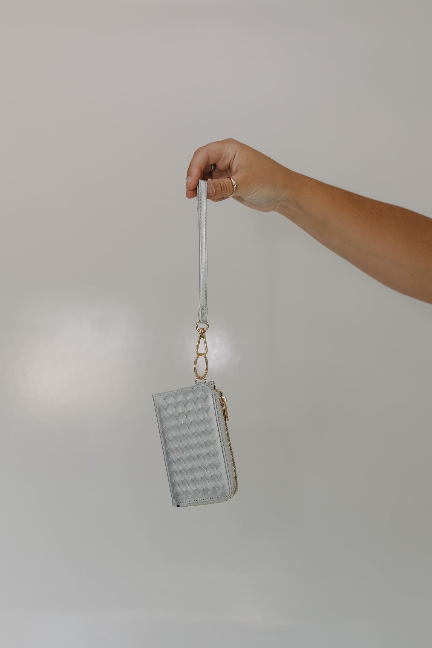 Hand holding a small textured wallet with a strap against a plain background
