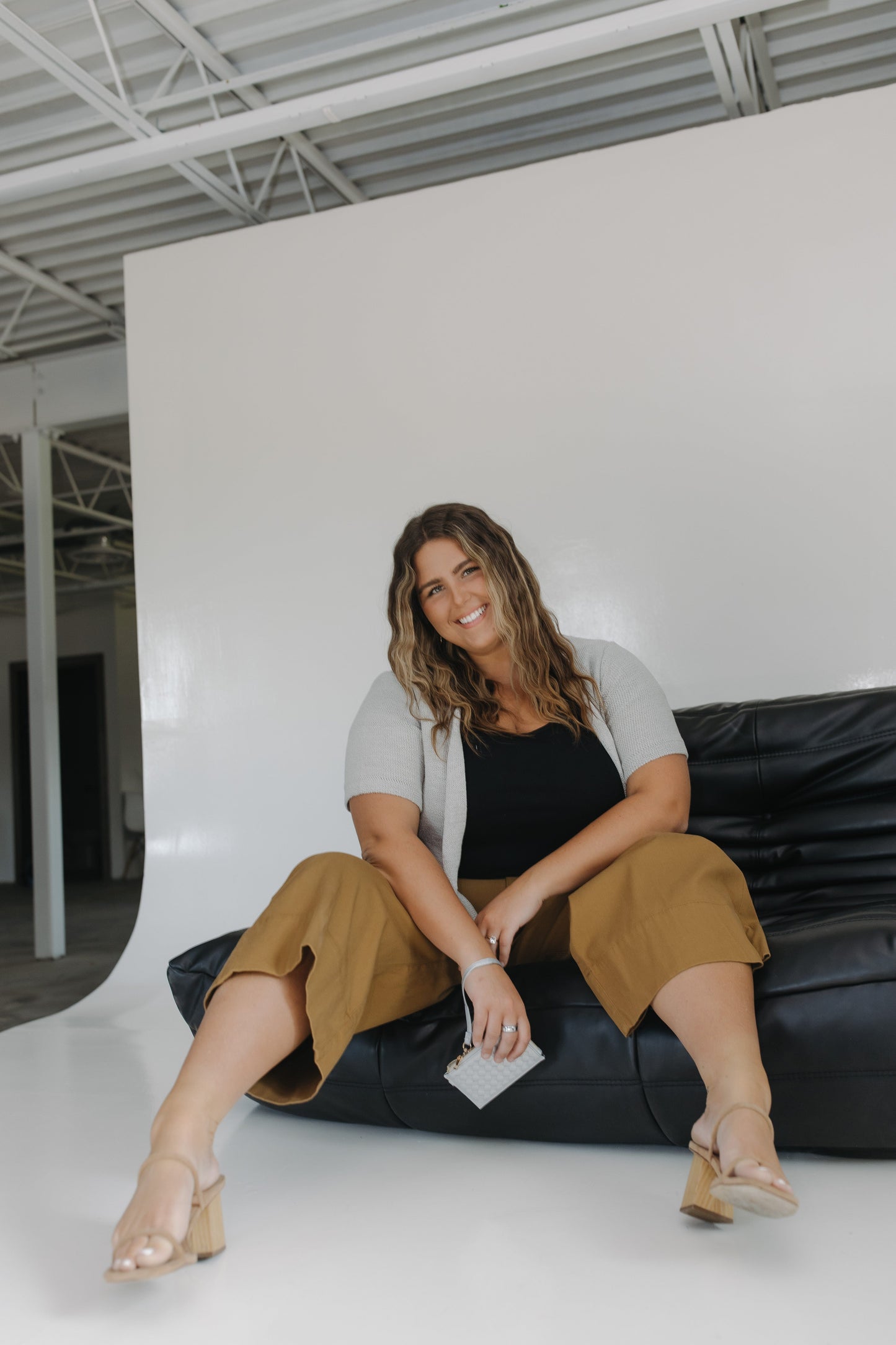Woman sitting in a cute outfit holding a silver woven wallet.