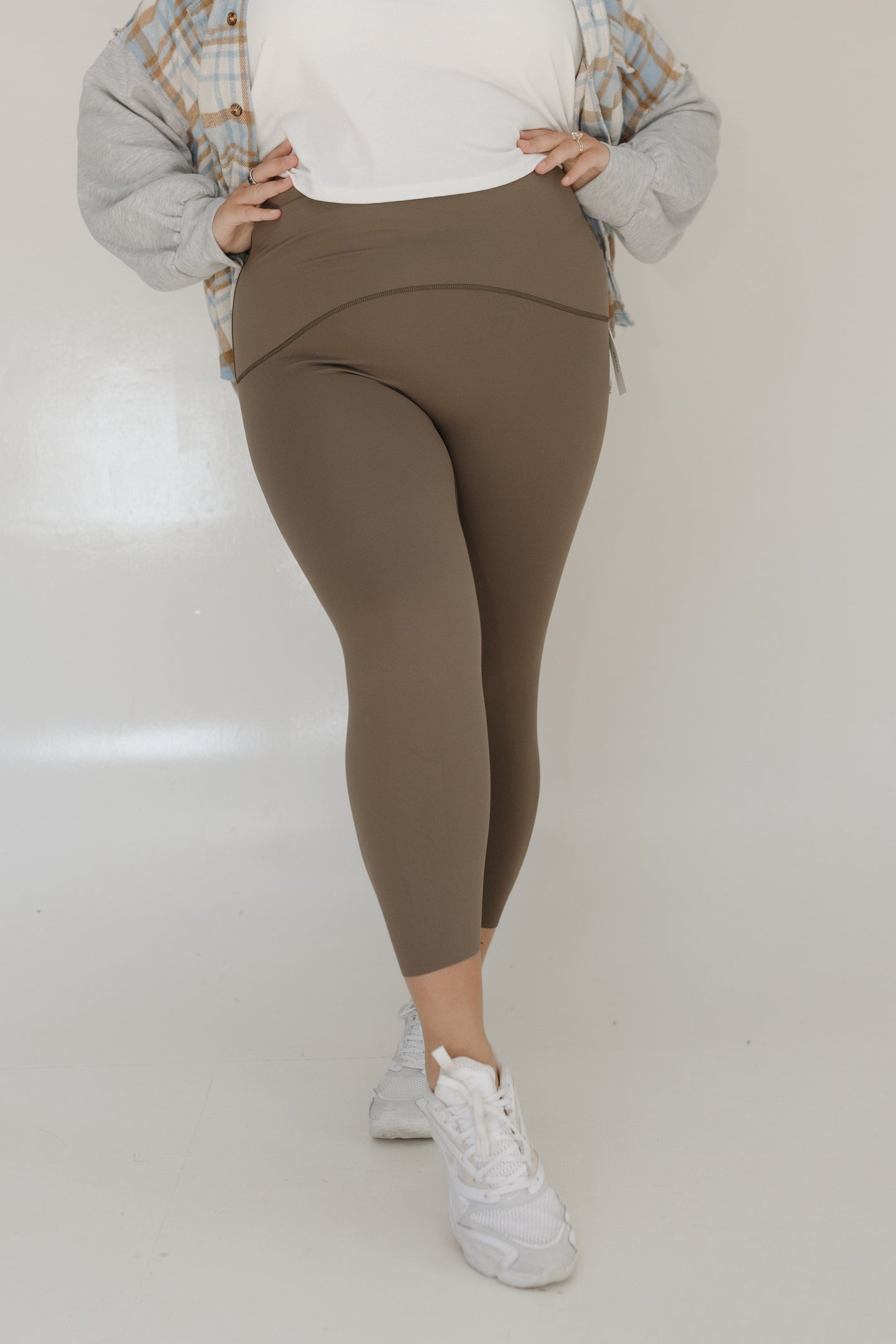 Person wearing brown leggings and white sneakers on a plain background