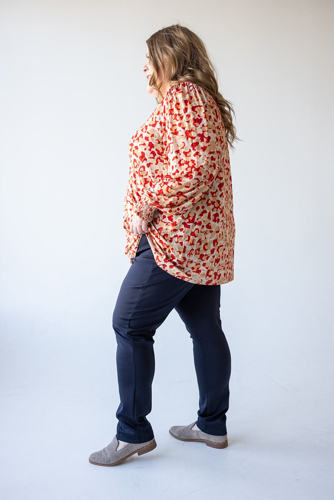 A person in a red patterned blouse and navy slim-straight-leg pants, made of luxurious sateen fabric, stands against a light background, facing left.