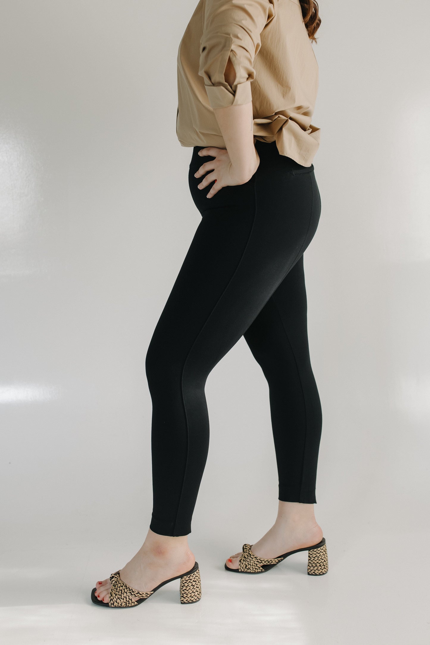 Person wearing black leggings and beige top on a white background